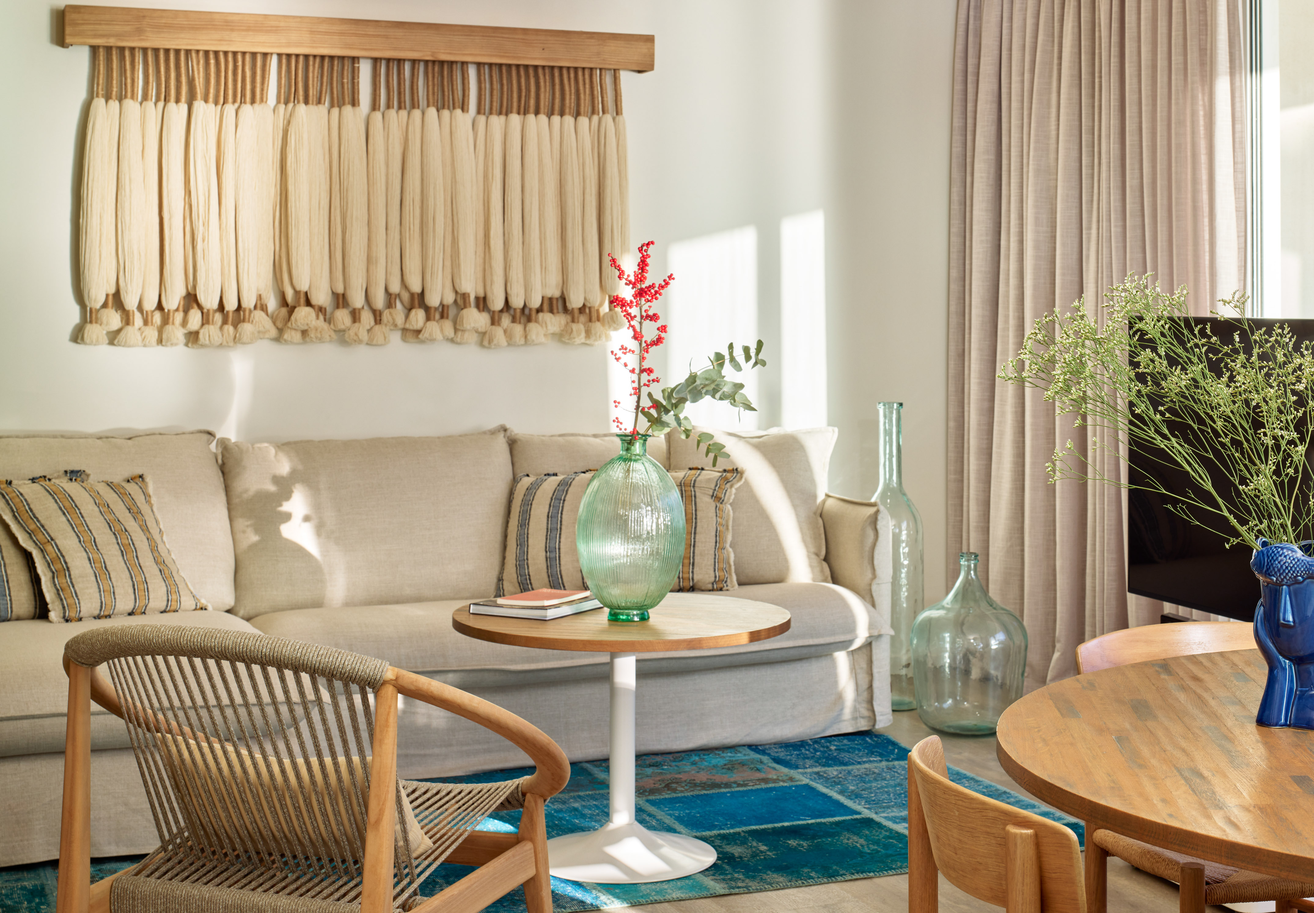 Bright bohemian living room with sofa, woven armchair, and wall tapestry.