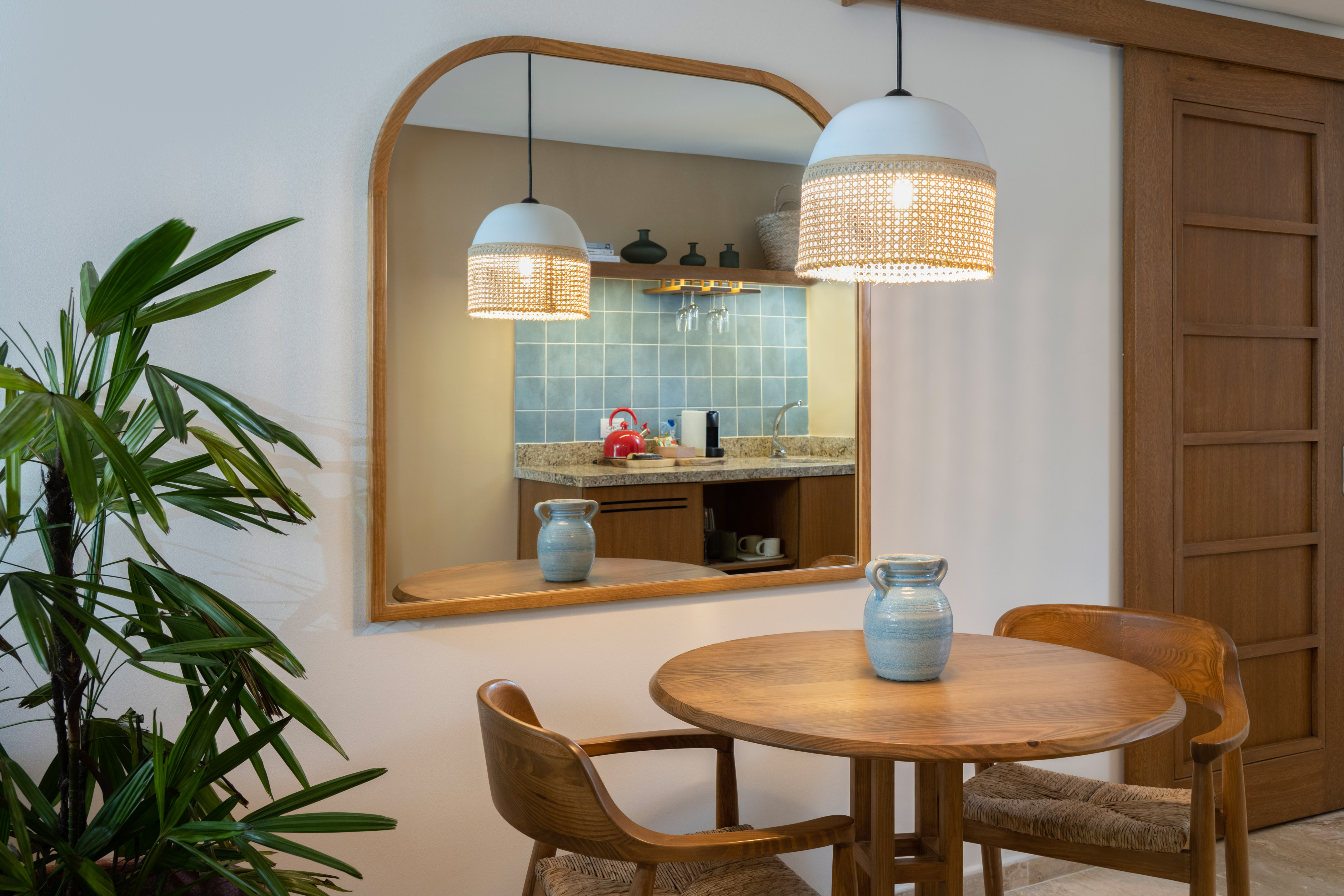 Wooden dining area, arch mirror reflecting kitchenette, rattan pendant lights.