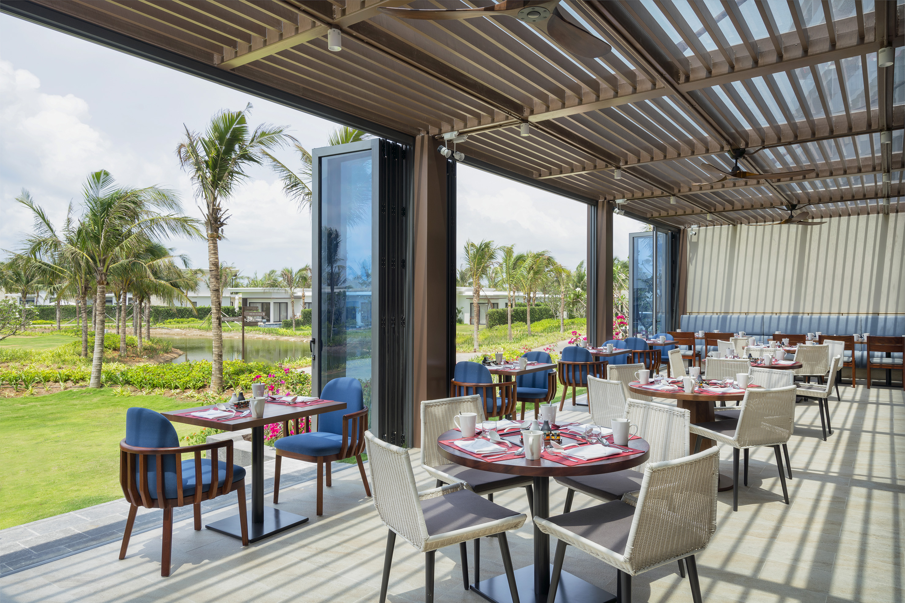 Tropical resort outdoor restaurant patio with dining tables and palm trees.