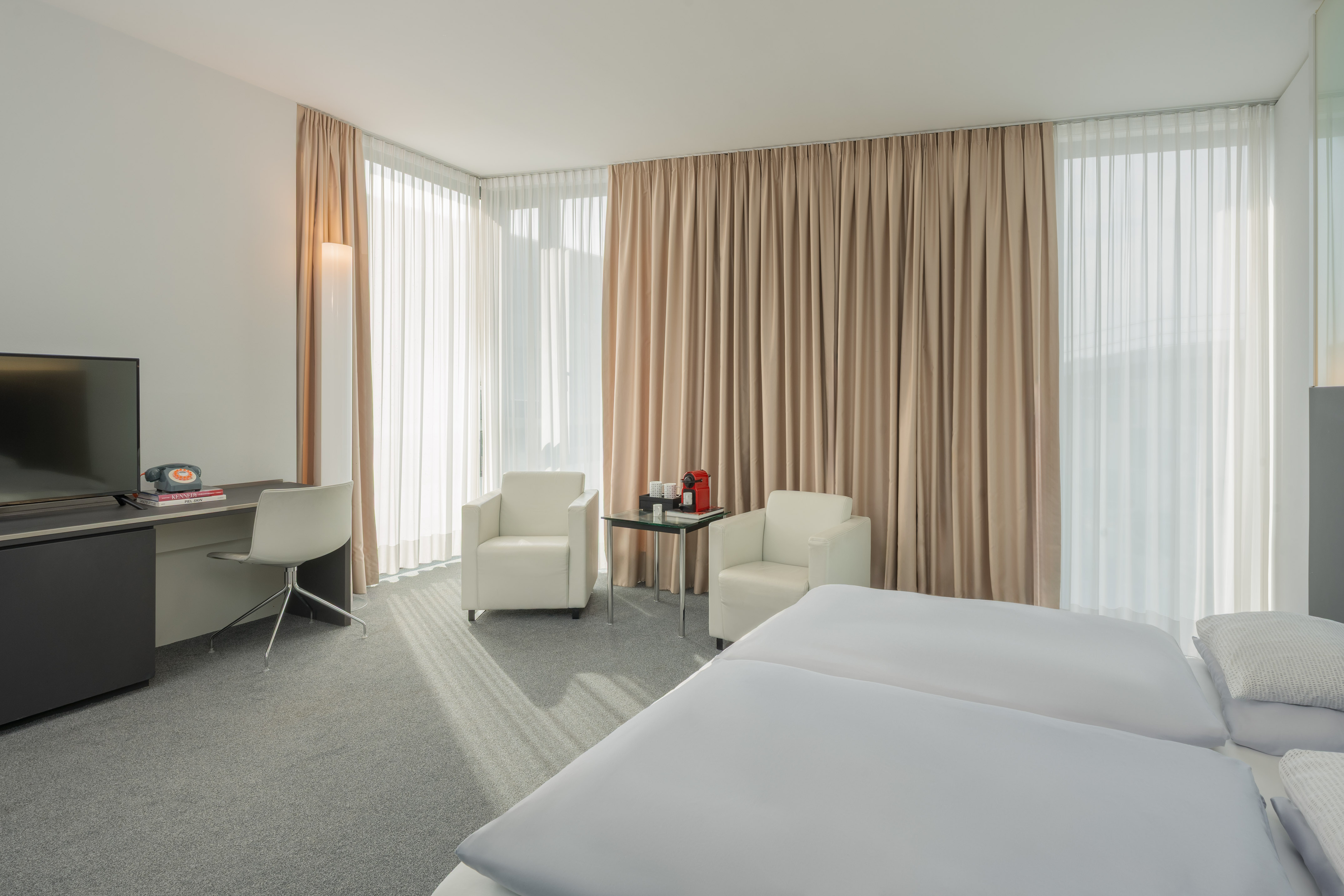 Bright modern hotel room with twin beds, work desk, and neutral decor.