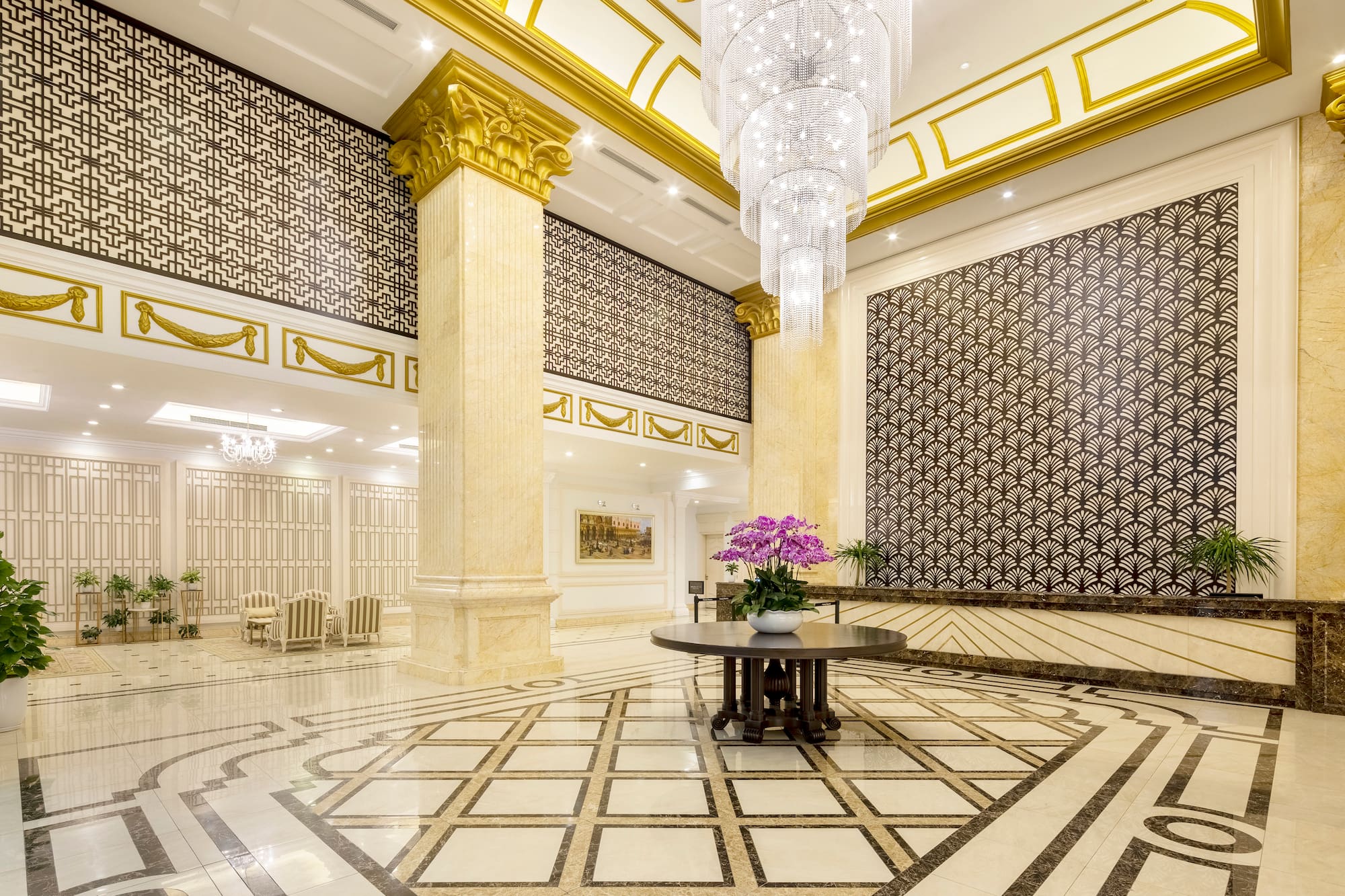 Grand luxury hotel lobby with crystal chandelier, gold decor, and patterned marble floor.