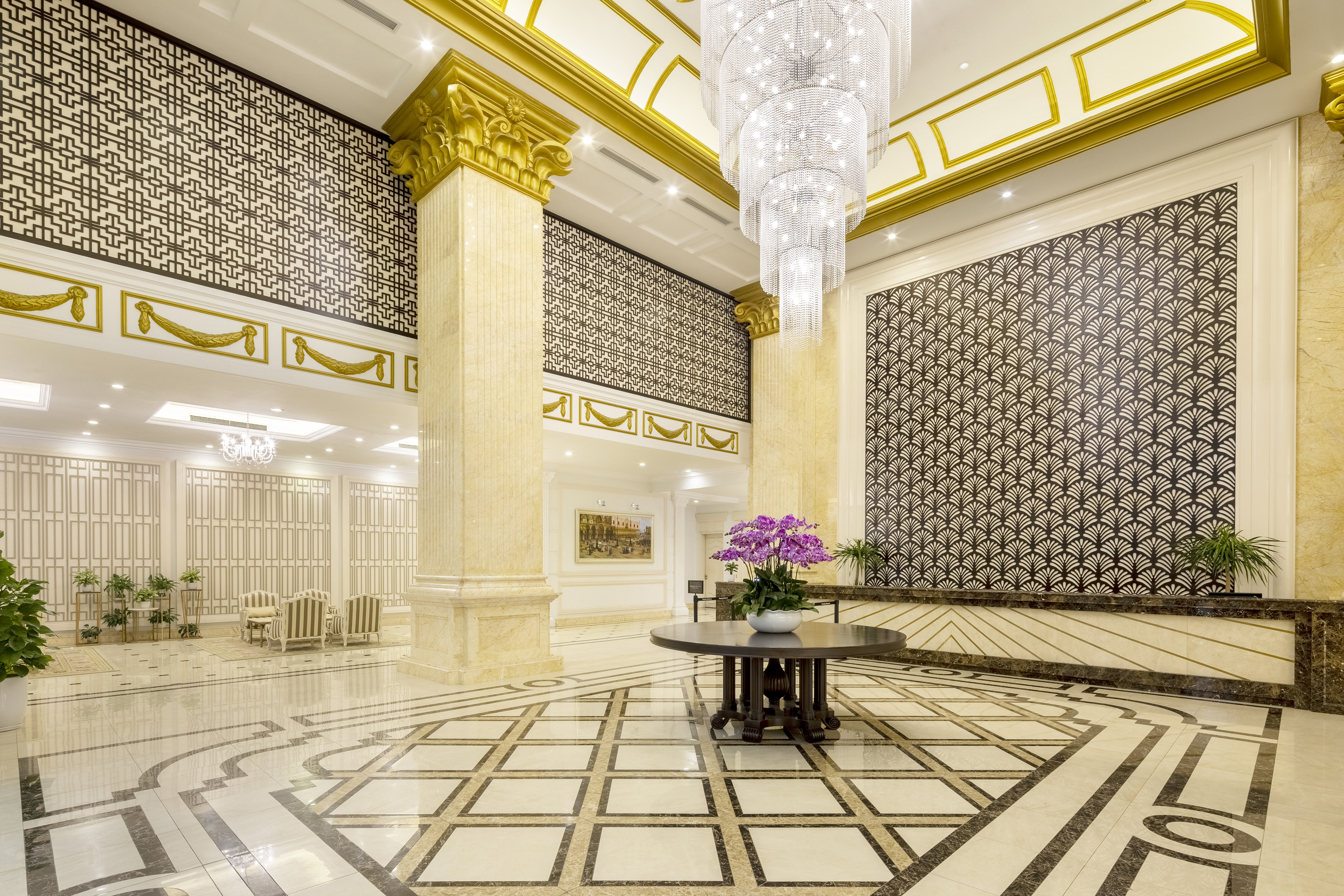 Grand luxury hotel lobby with crystal chandelier, gold decor, and patterned marble floor.