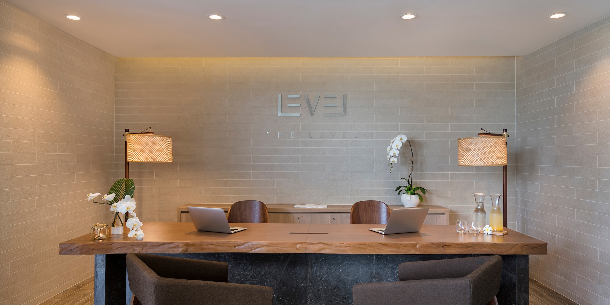 Modern 'THE LEVEL' hotel reception desk with wood top, laptops, and orchids.