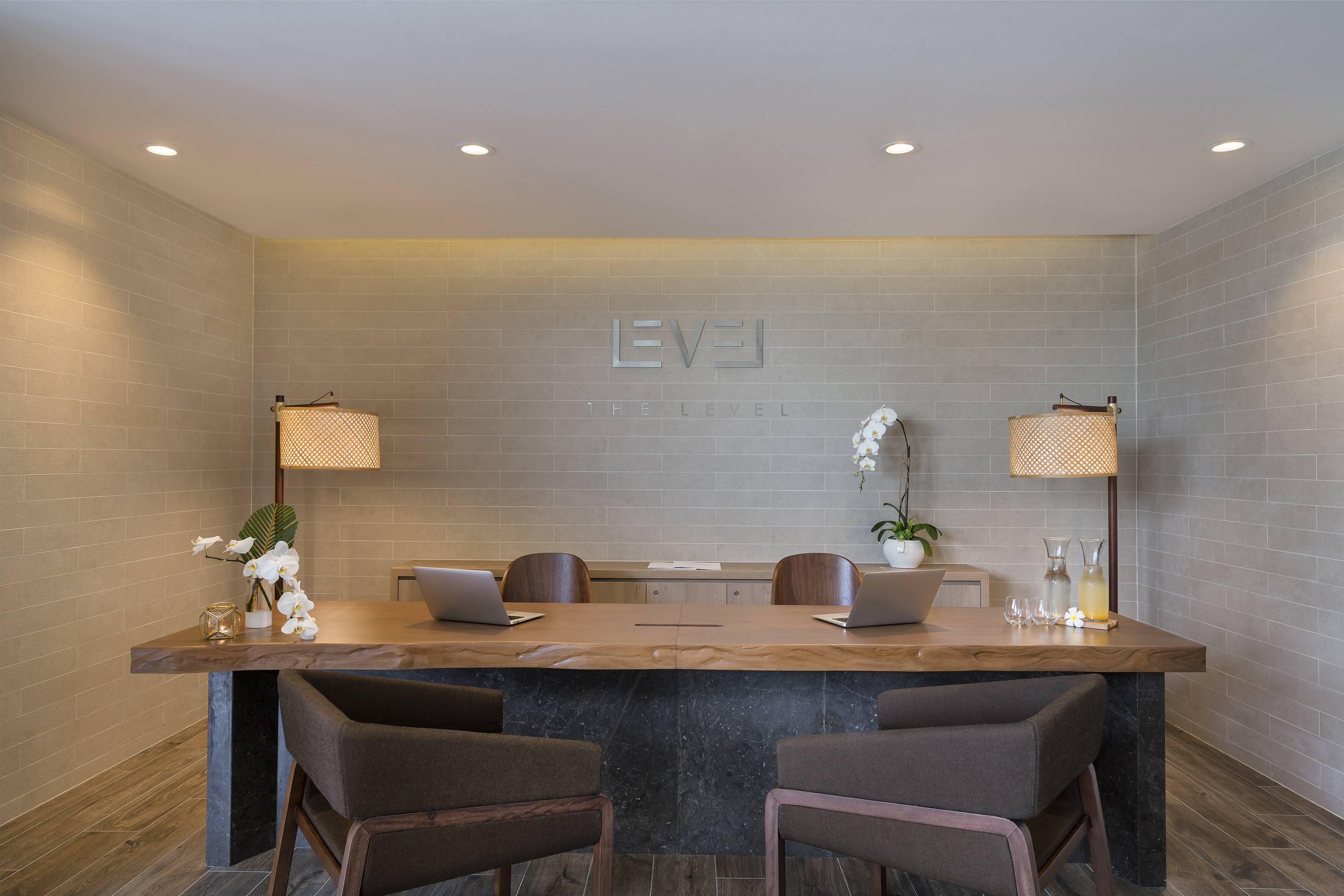 Modern 'THE LEVEL' hotel reception desk with wood top, laptops, and orchids.