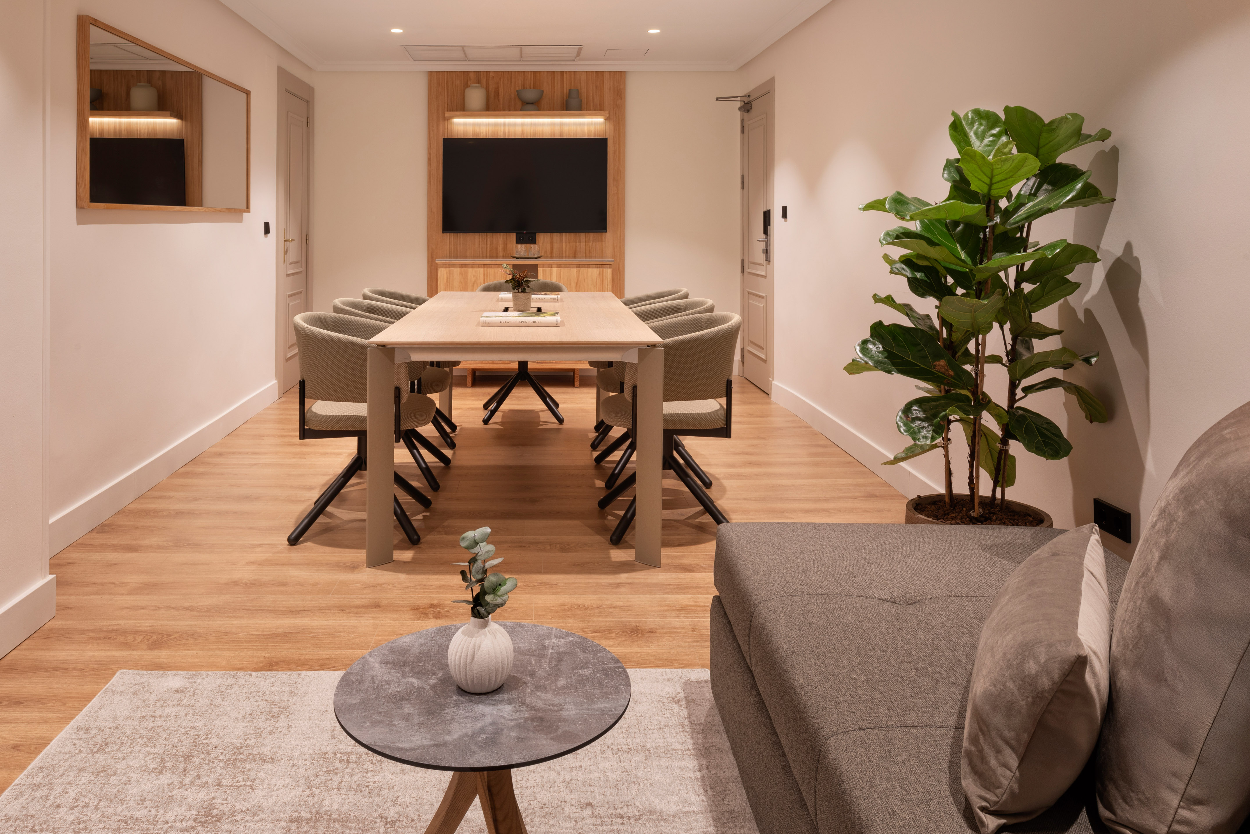 Modern conference room with table, chairs, TV, and adjacent lounge seating.