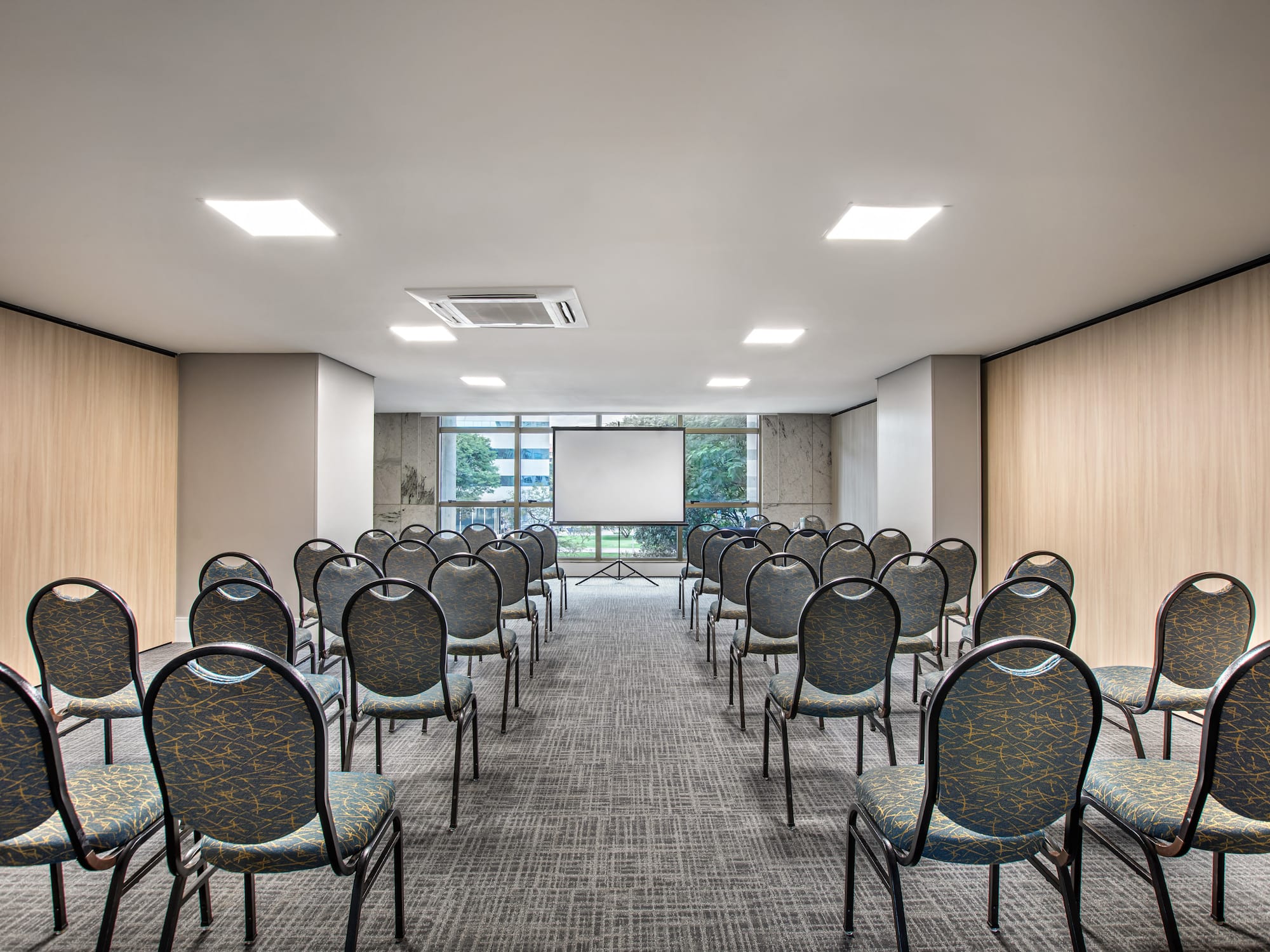 Conference room with projection screen, rows of patterned chairs, and wood walls.