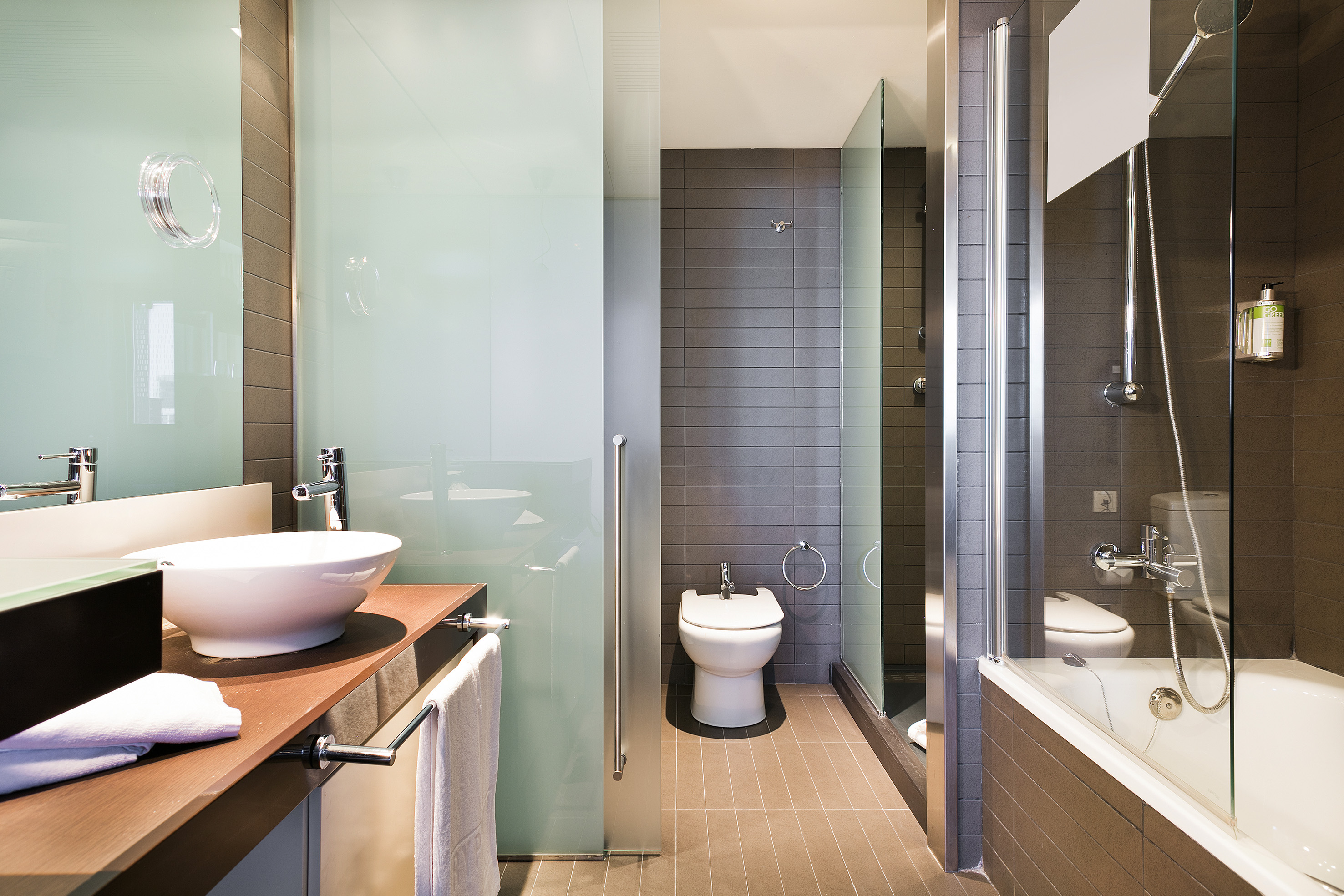 Modern hotel bathroom with glass shower, vessel sink, toilet, and bidet.