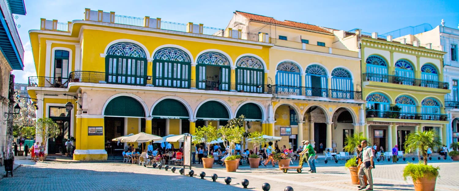 a yellow building with many people and a yellow building with many windows with Willemstad in the background