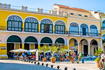 a yellow building with many people and a yellow building with many windows with Willemstad in the background