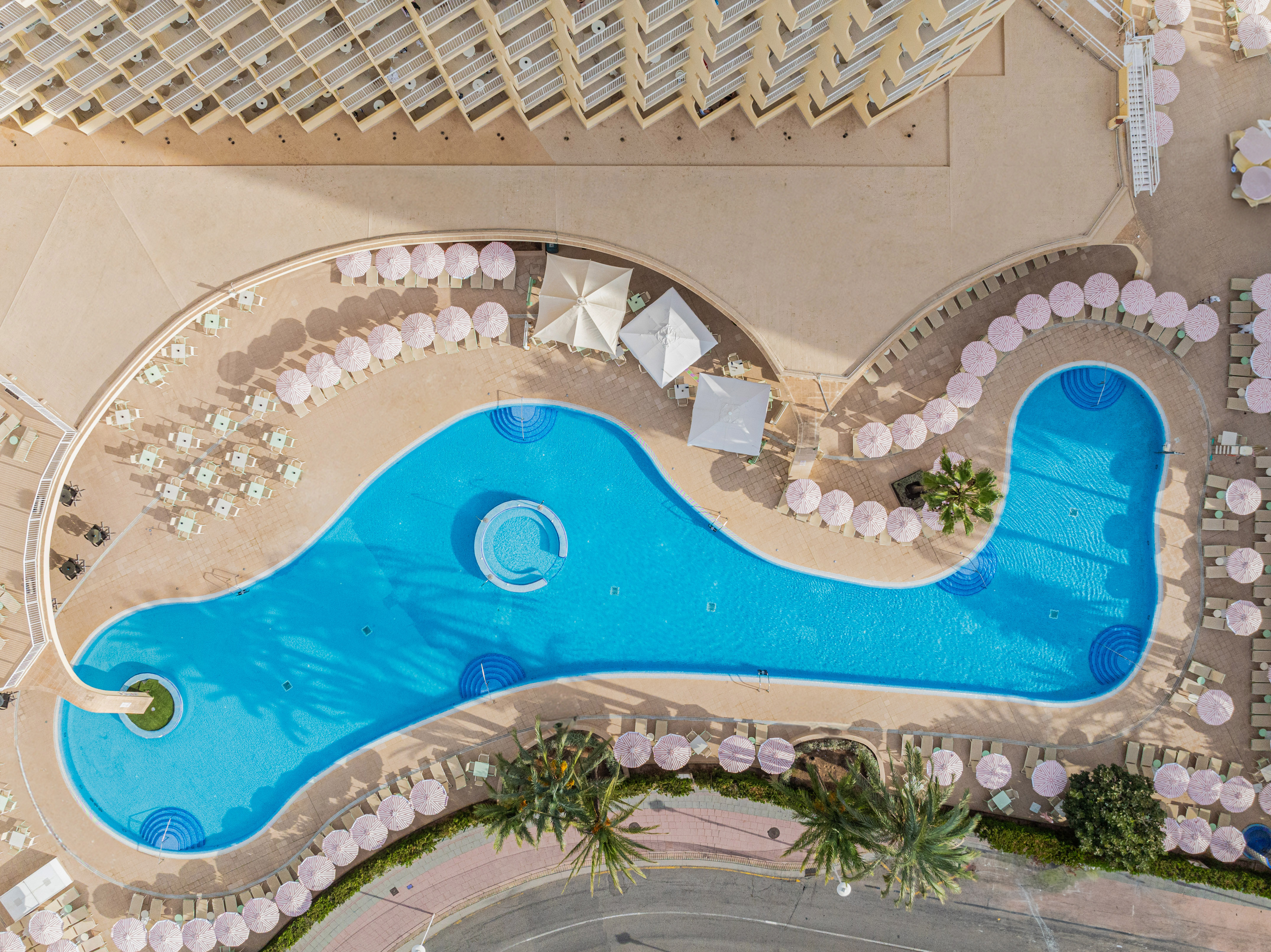Aerial view of hotel resort pool with pink umbrellas and loungers.