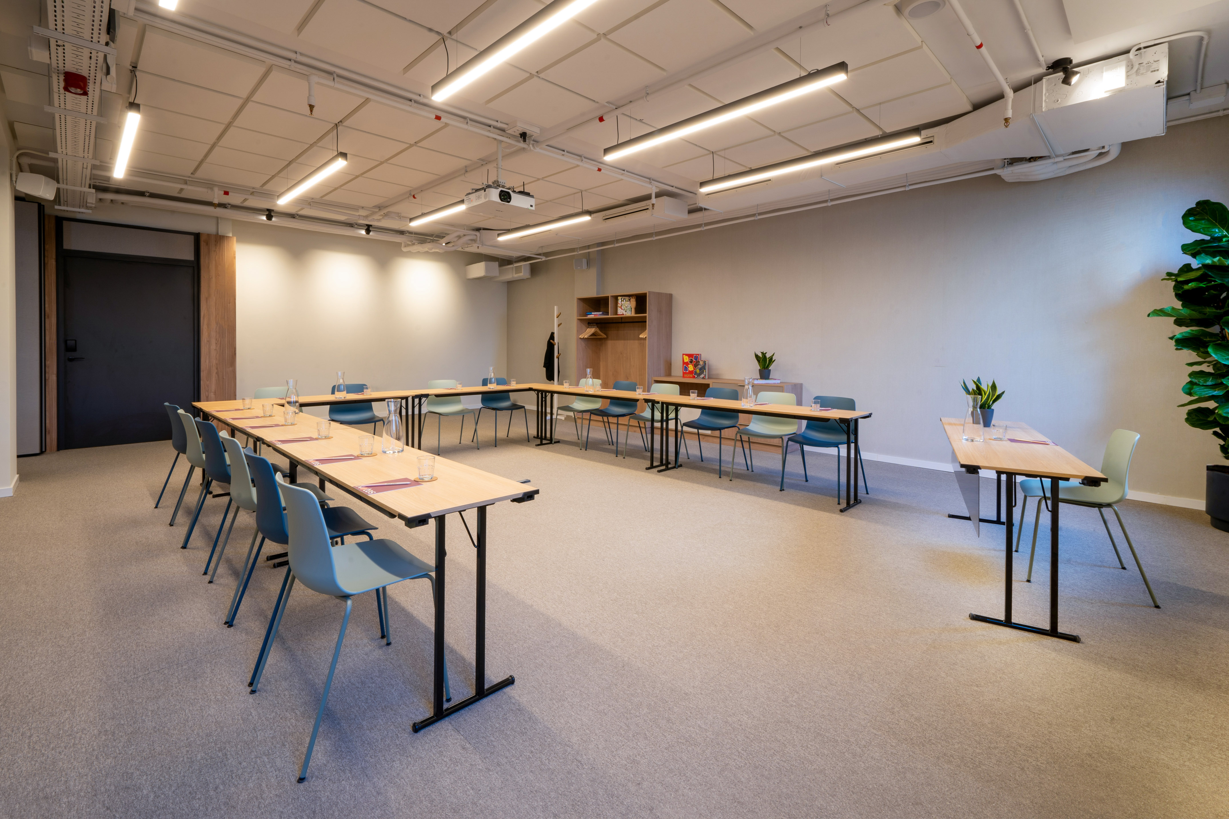 Modern meeting room with U-shaped tables, blue chairs, and ceiling projector.