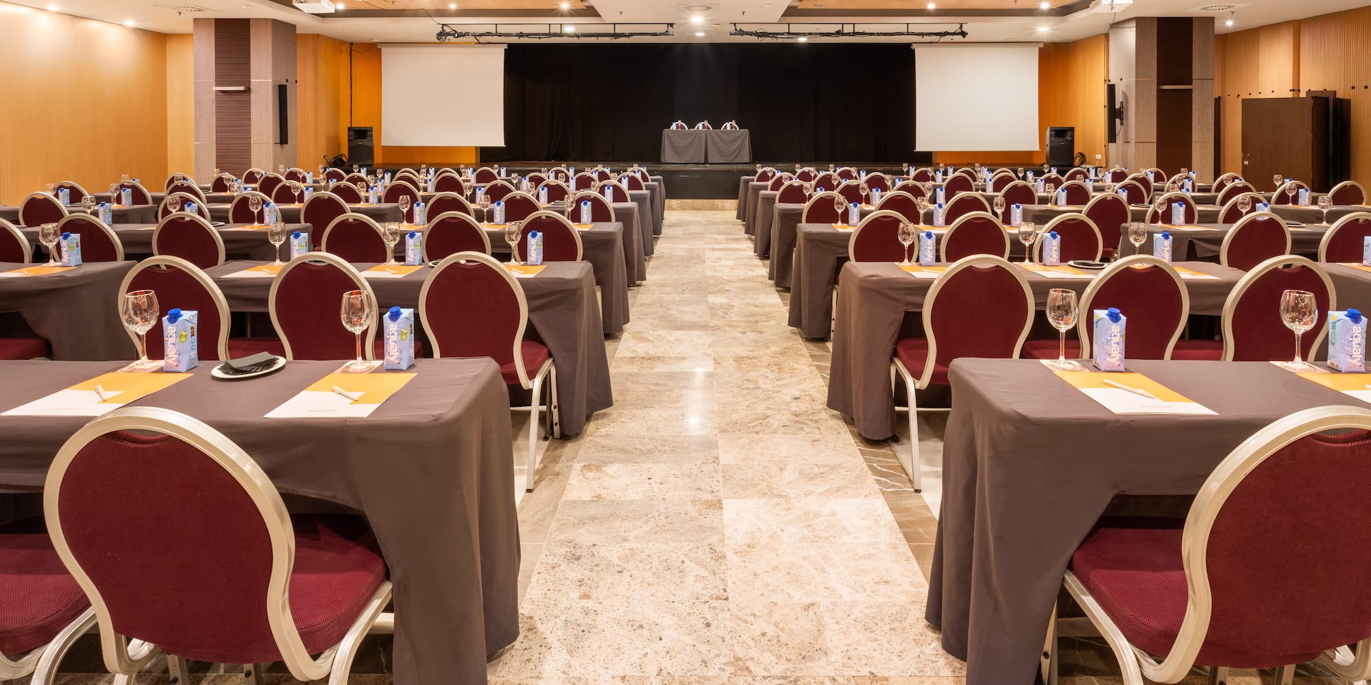 Empty hotel conference room setup with rows of tables, chairs, and stage.