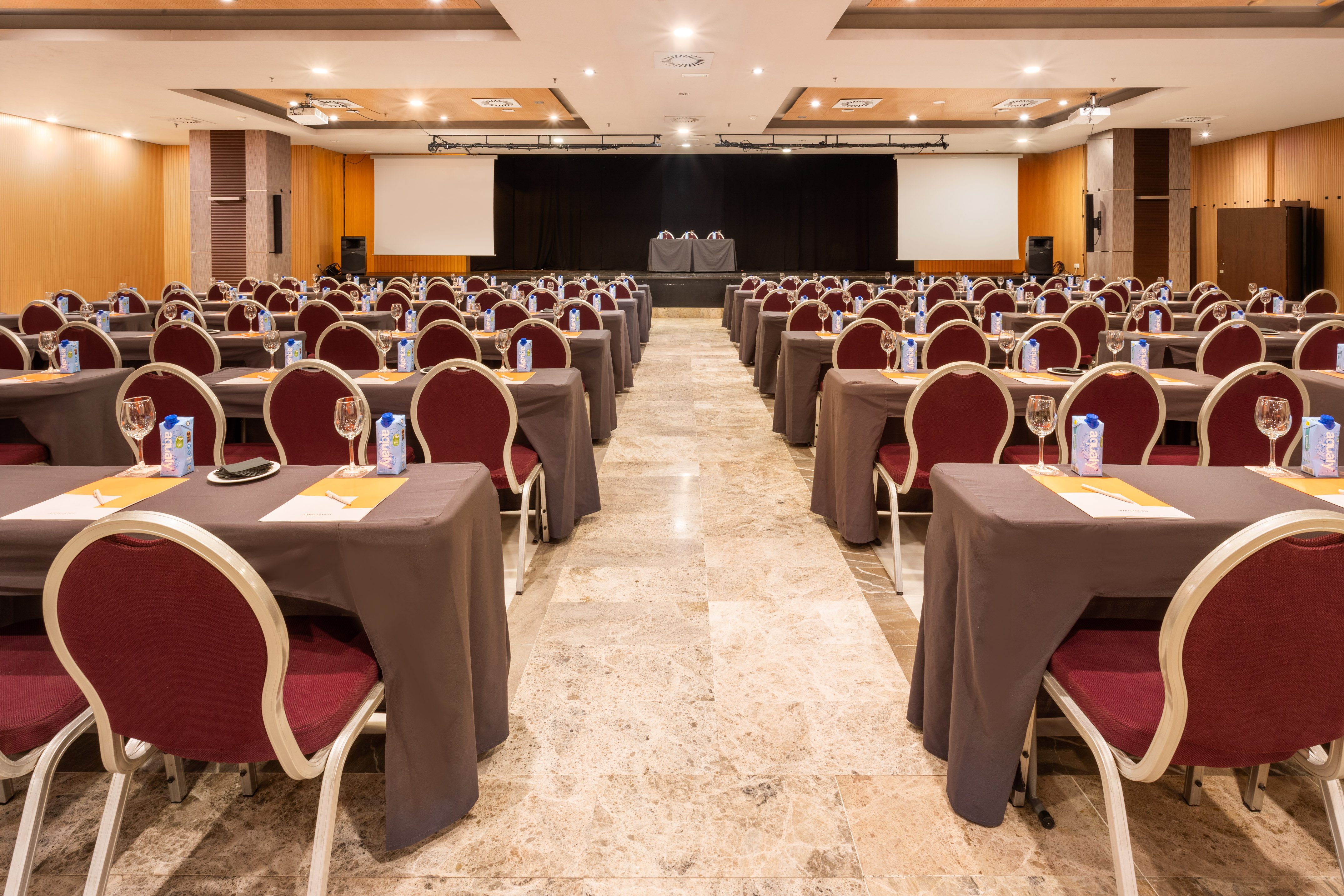 Empty hotel conference room setup with rows of tables, chairs, and stage.