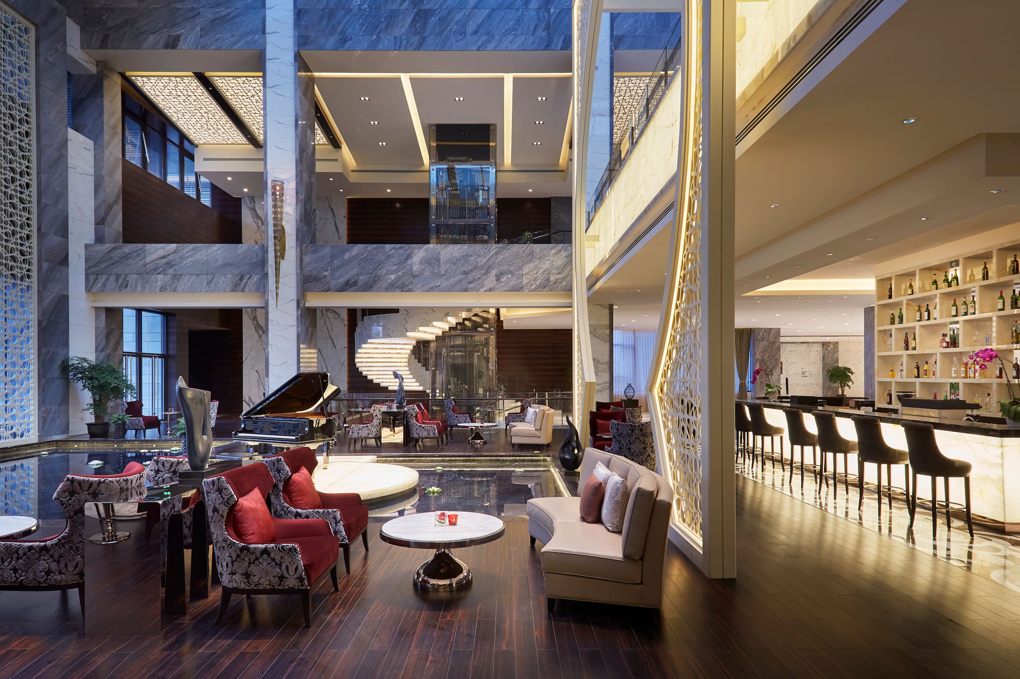 Grand hotel lobby with piano, spiral staircase, bar, and modern seating area.