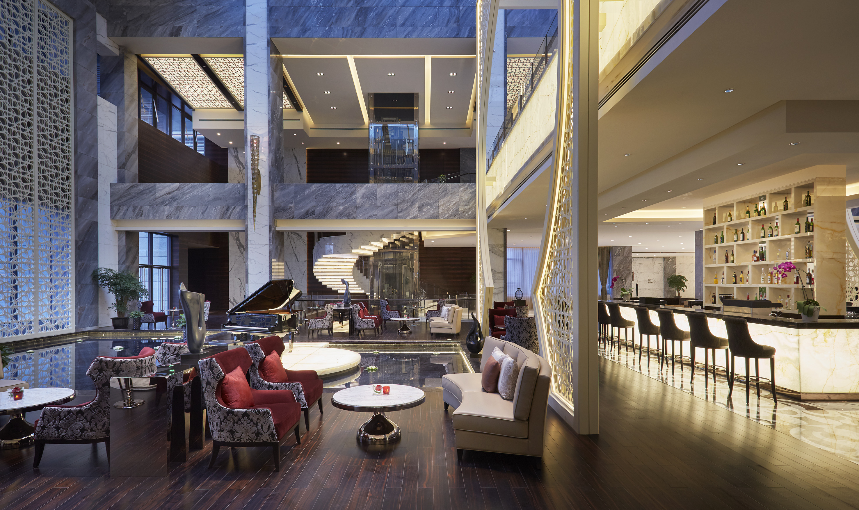 Grand hotel lobby with piano, spiral staircase, bar, and modern seating area.
