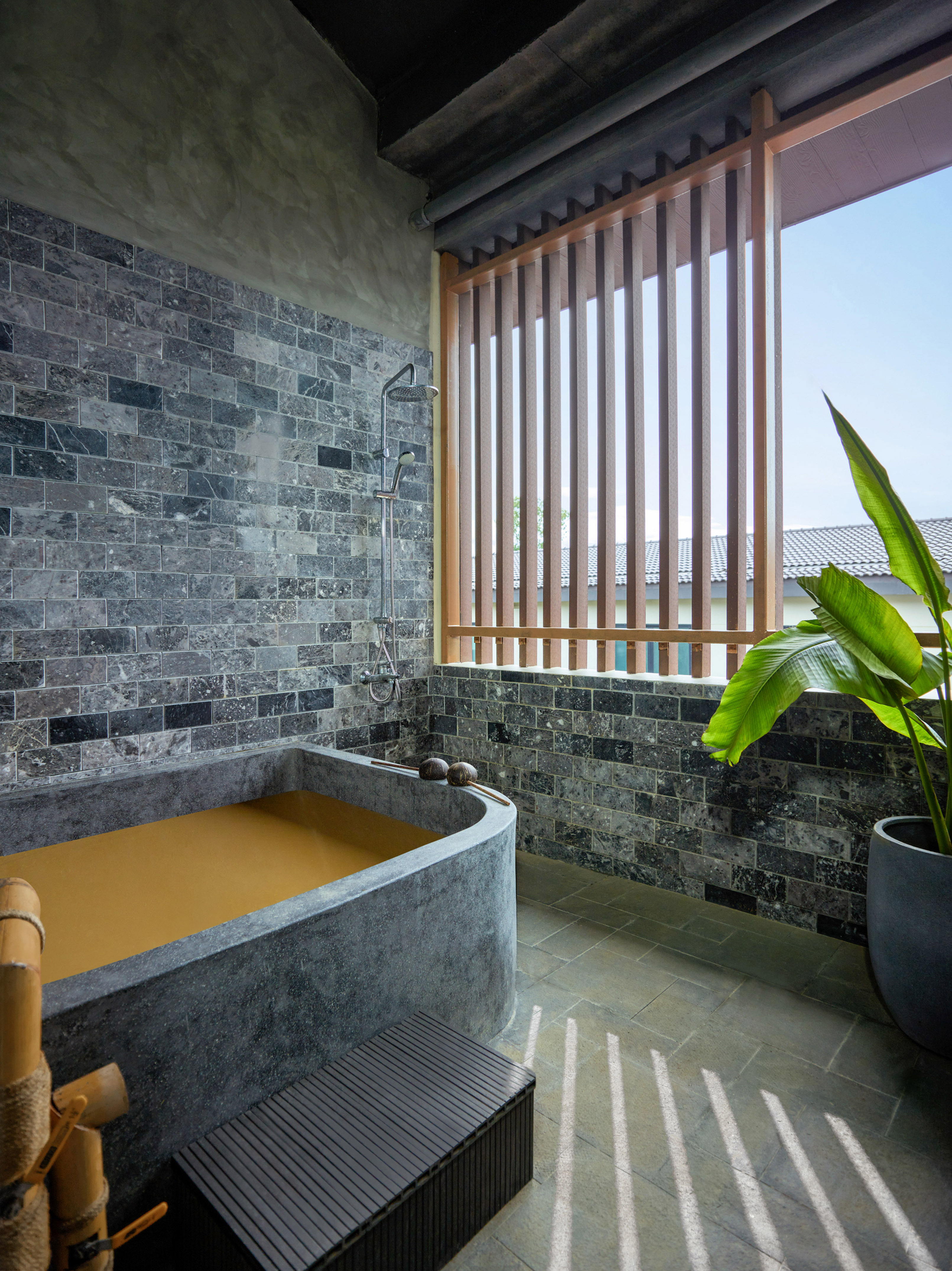 Outdoor stone mud bath with shower, tiled wall, and wooden privacy screen.