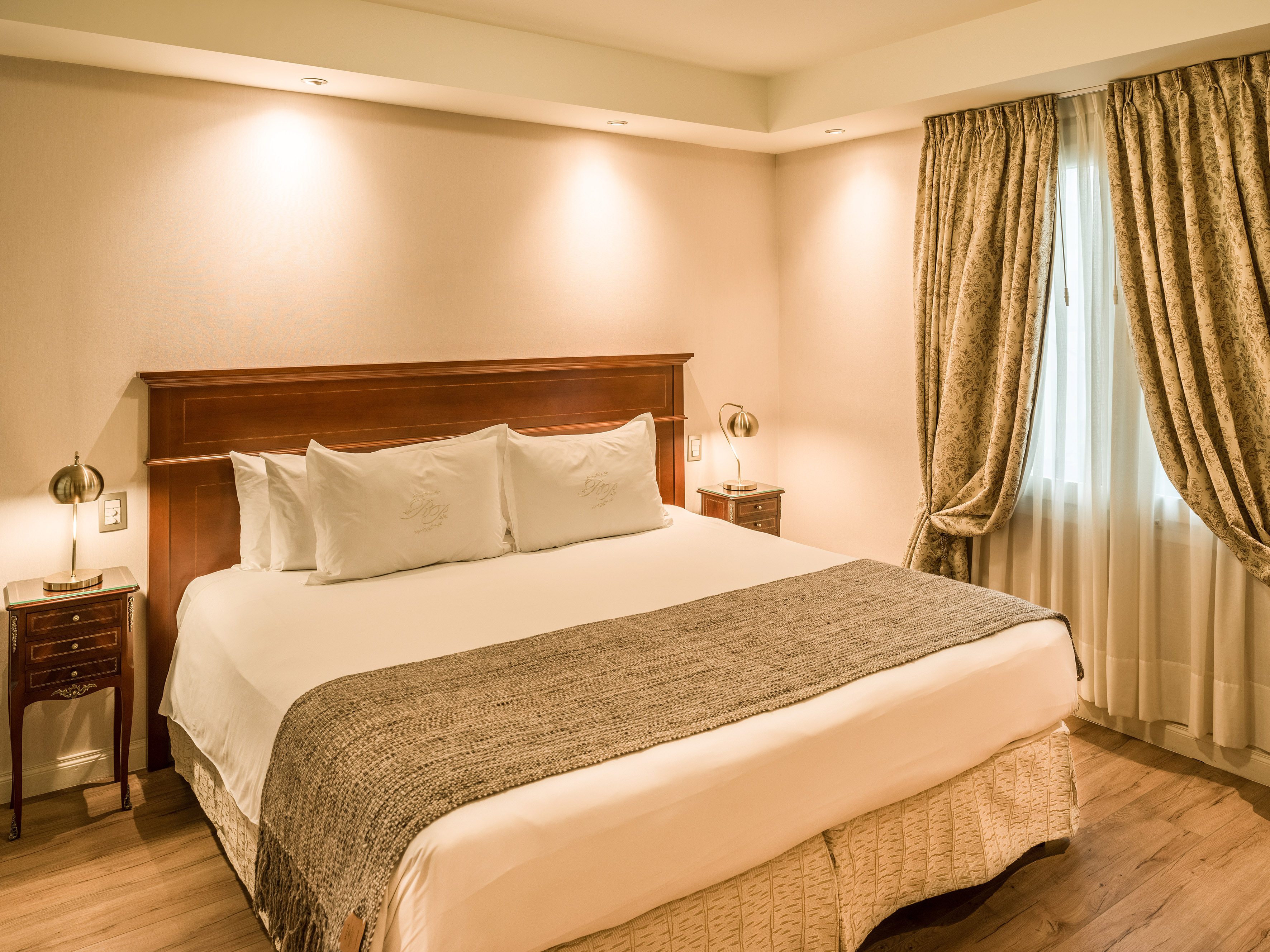 Hotel bedroom with large bed, wooden headboard, nightstands, and patterned curtains.