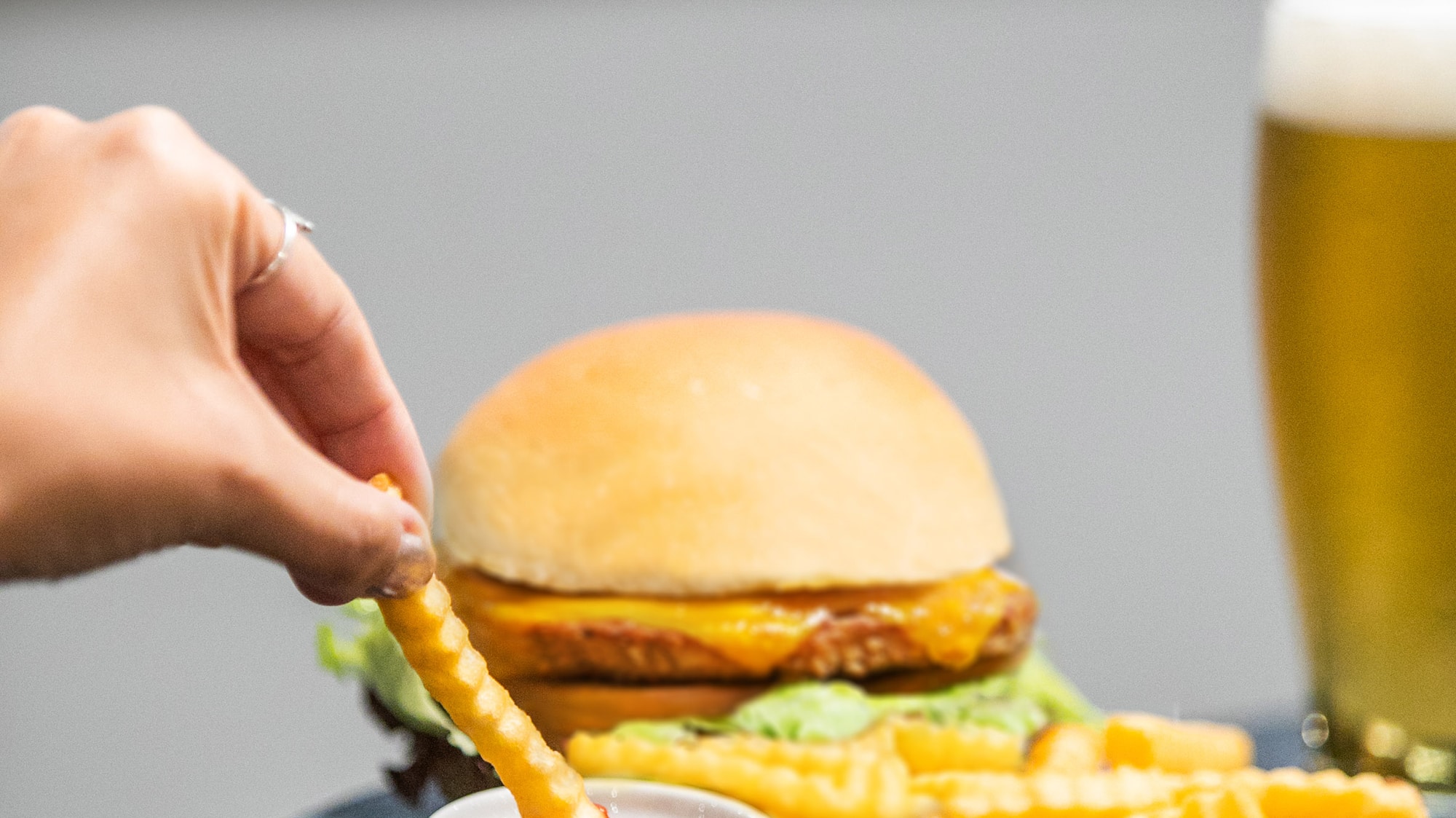 a hand dipping a french fries into a burger