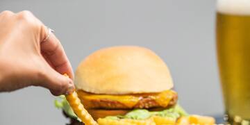 a hand dipping a french fries into a burger