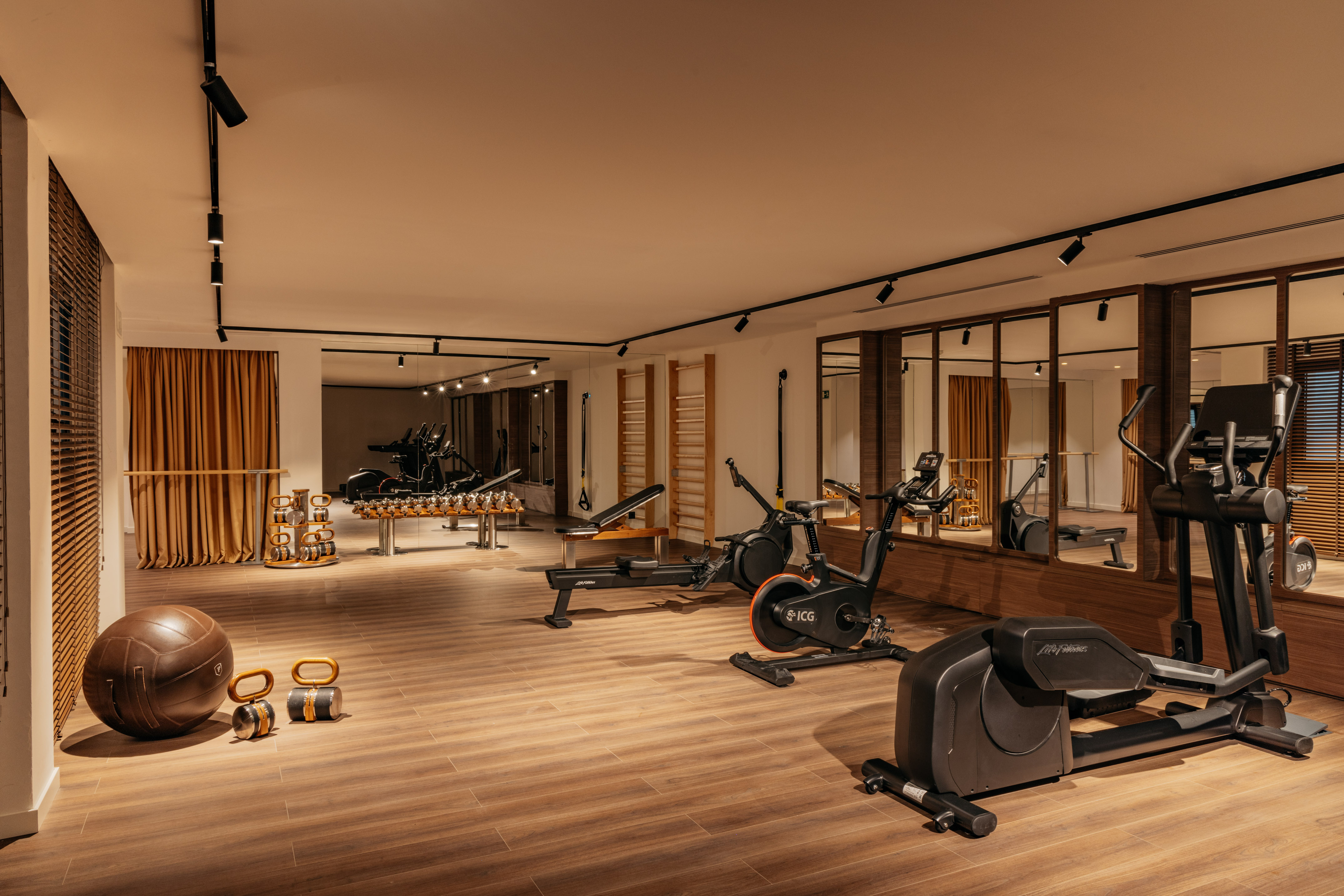 Modern fitness room with cardio machines, free weights, and mirrored walls.