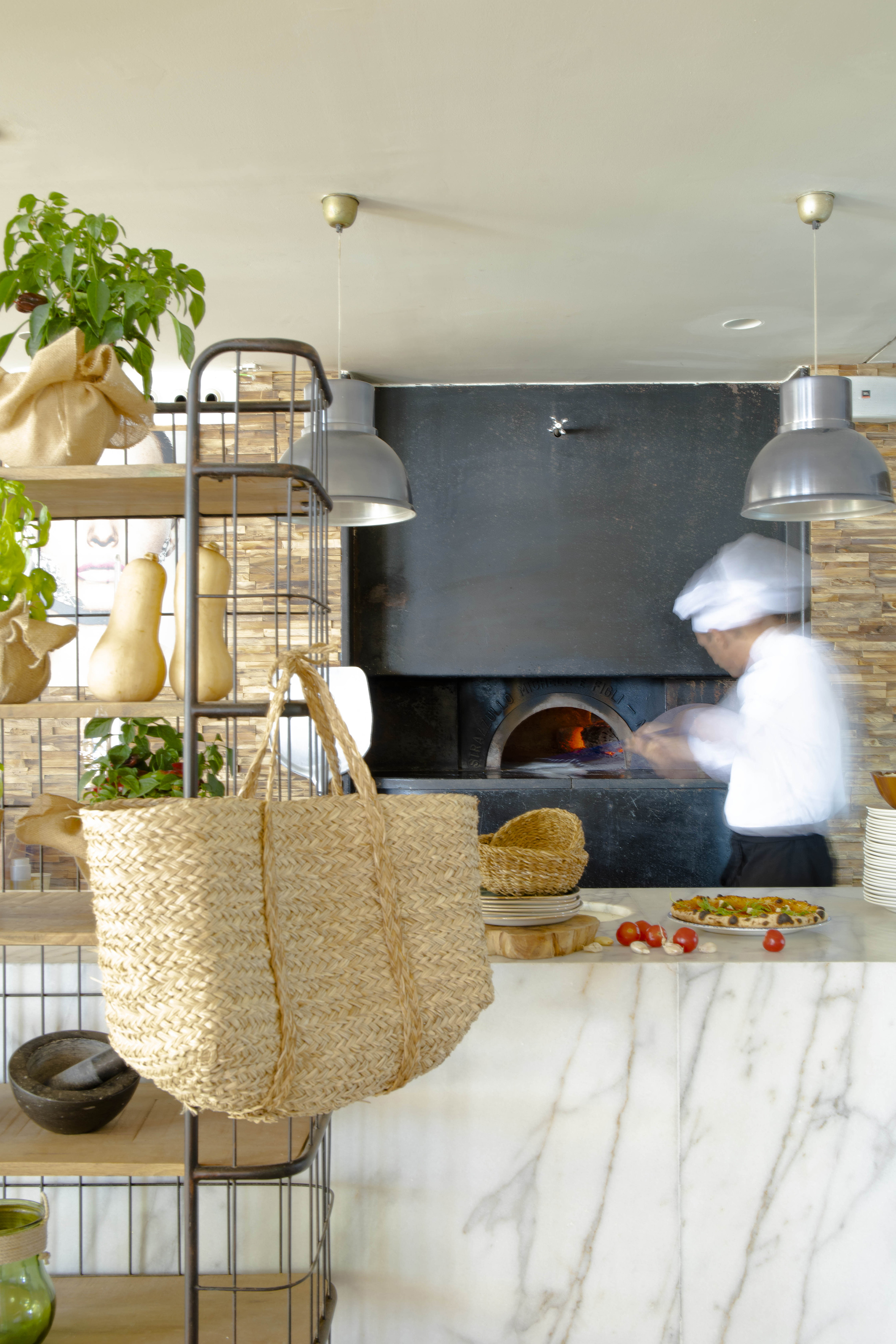 Motion-blurred chef cooking pizza at wood-fired oven, marble counter.