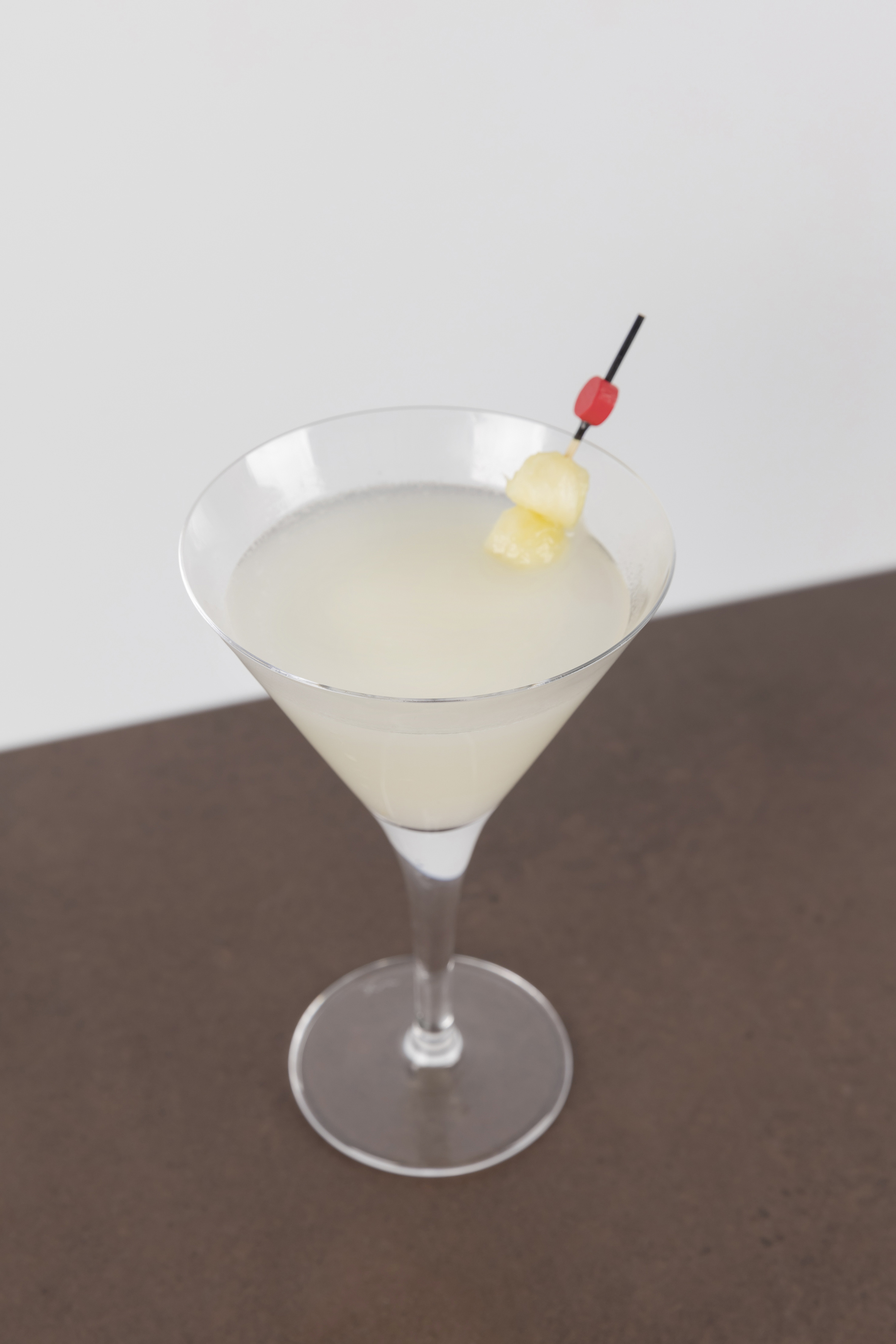 Martini glass with light cocktail and pineapple skewer.