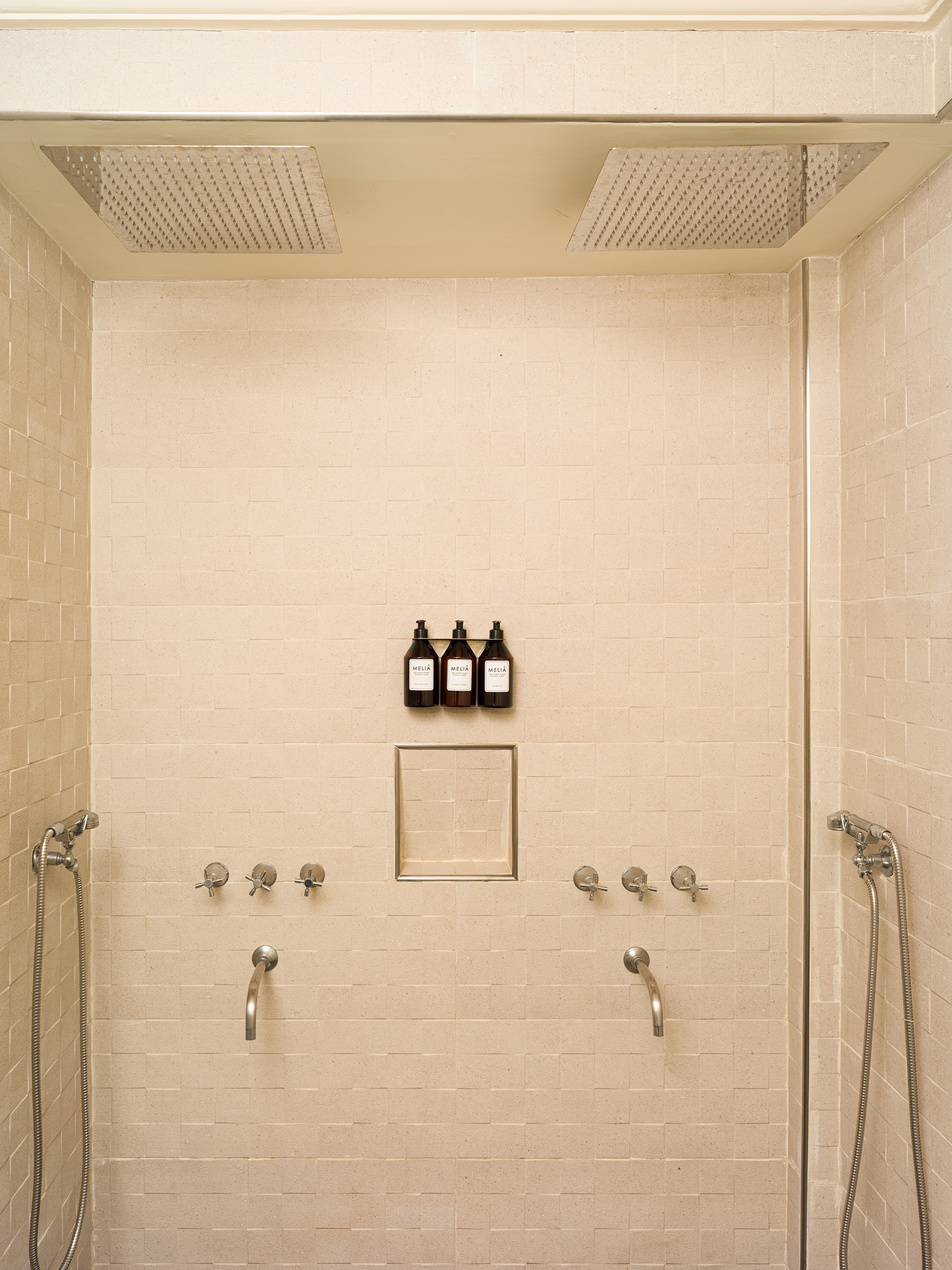 Spacious modern shower with dual rain heads, beige tiles, and Melia amenities.