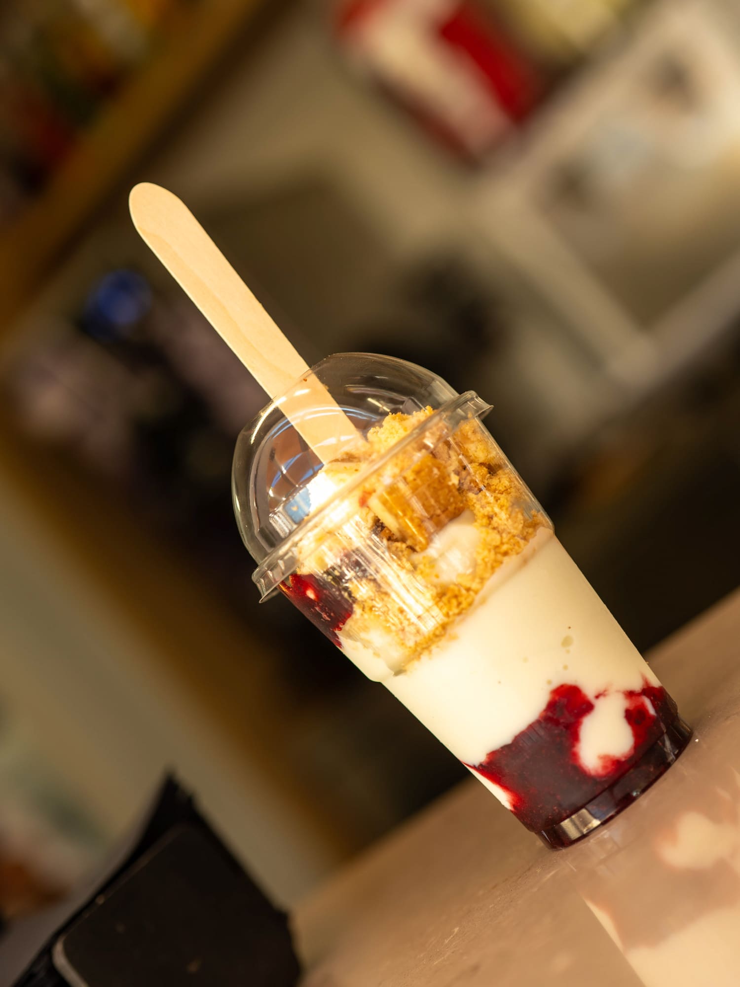 Dessert cup with berry layers, cream, and cookie crumbs, wooden spoon.