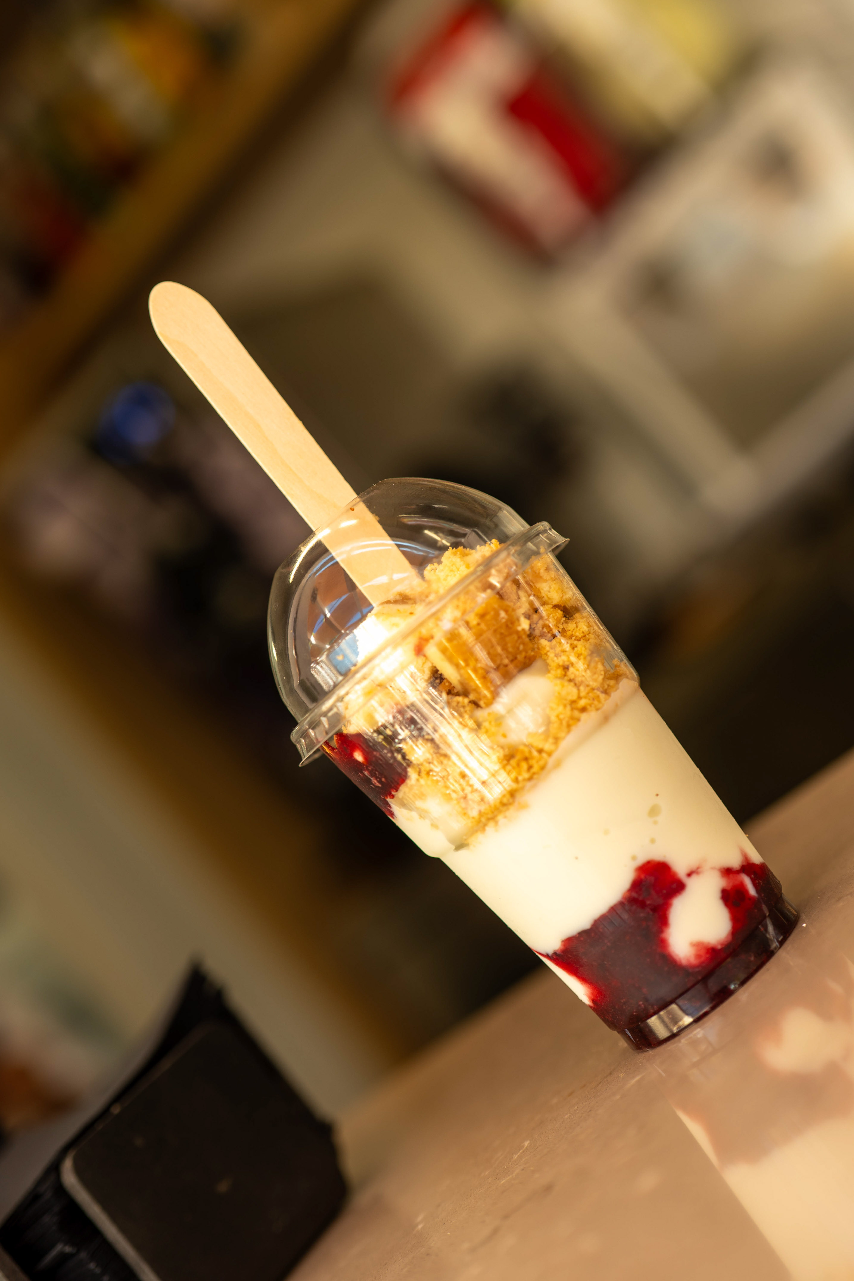 Dessert cup with berry layers, cream, and cookie crumbs, wooden spoon.
