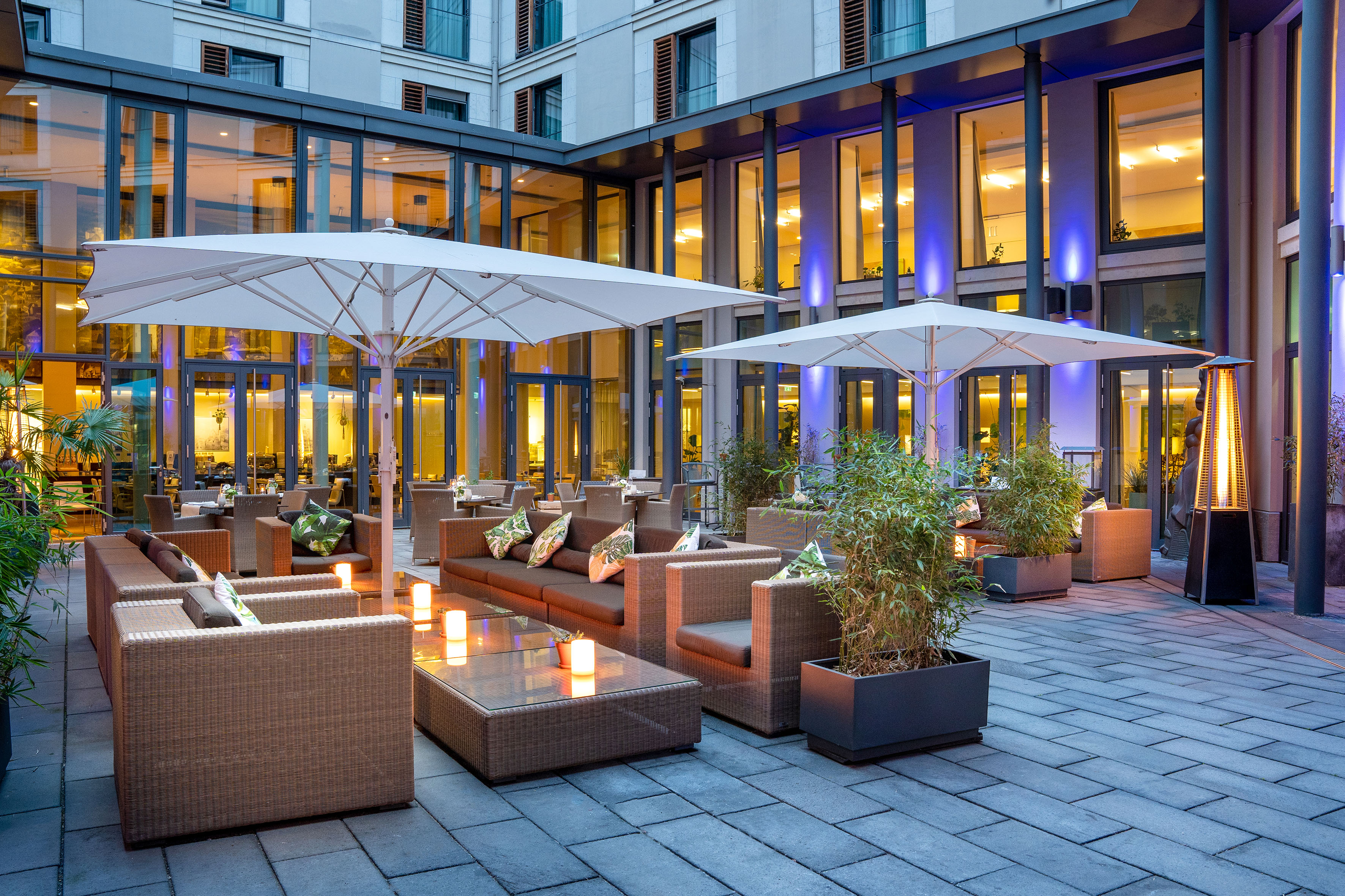 Modern hotel patio lounge with wicker furniture, umbrellas, ambient light. - VEN Patio - Innside Dresda, Dresda