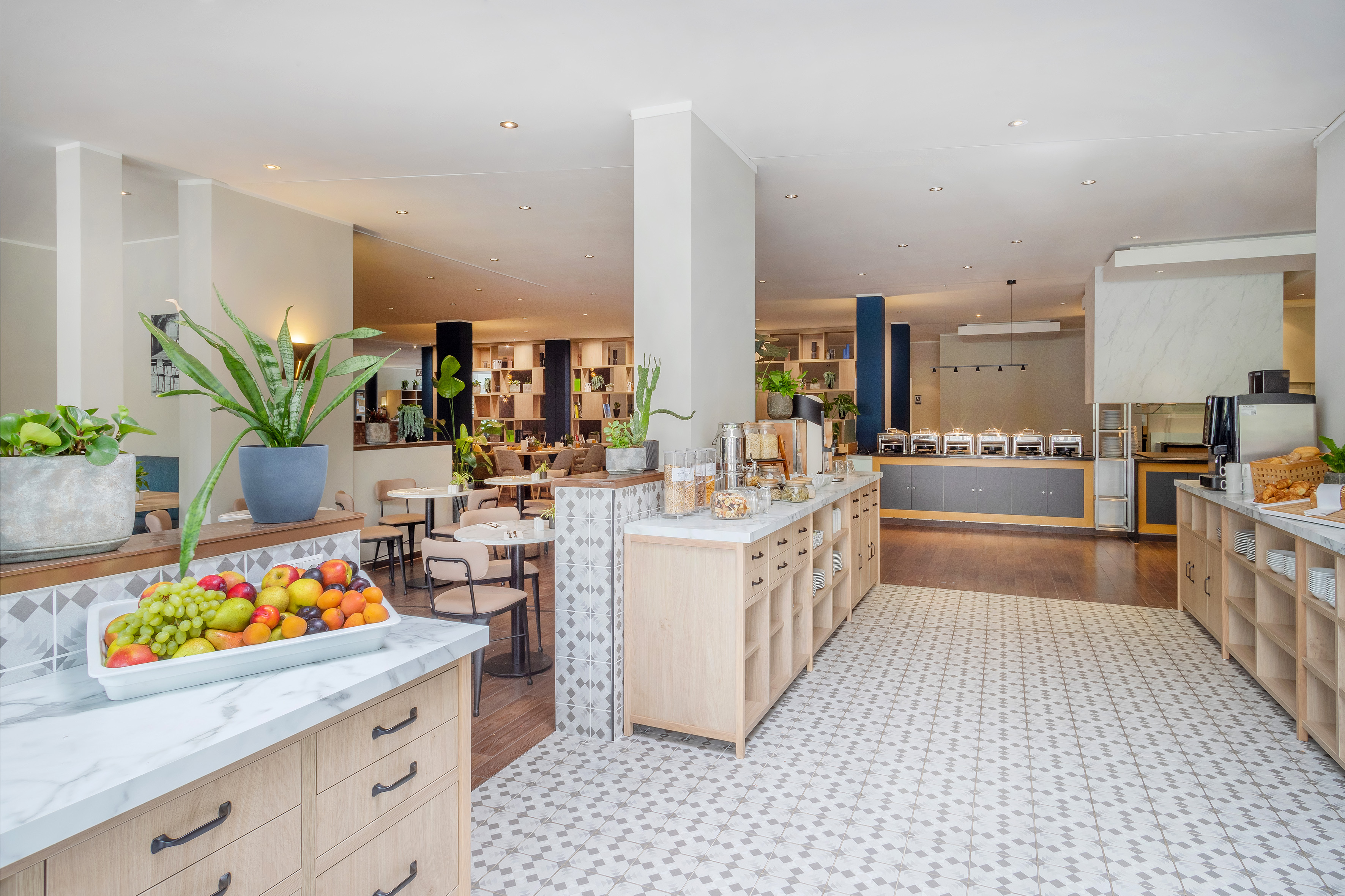 Modern hotel breakfast buffet with fresh fruit, cereals, hot food, and dining area.