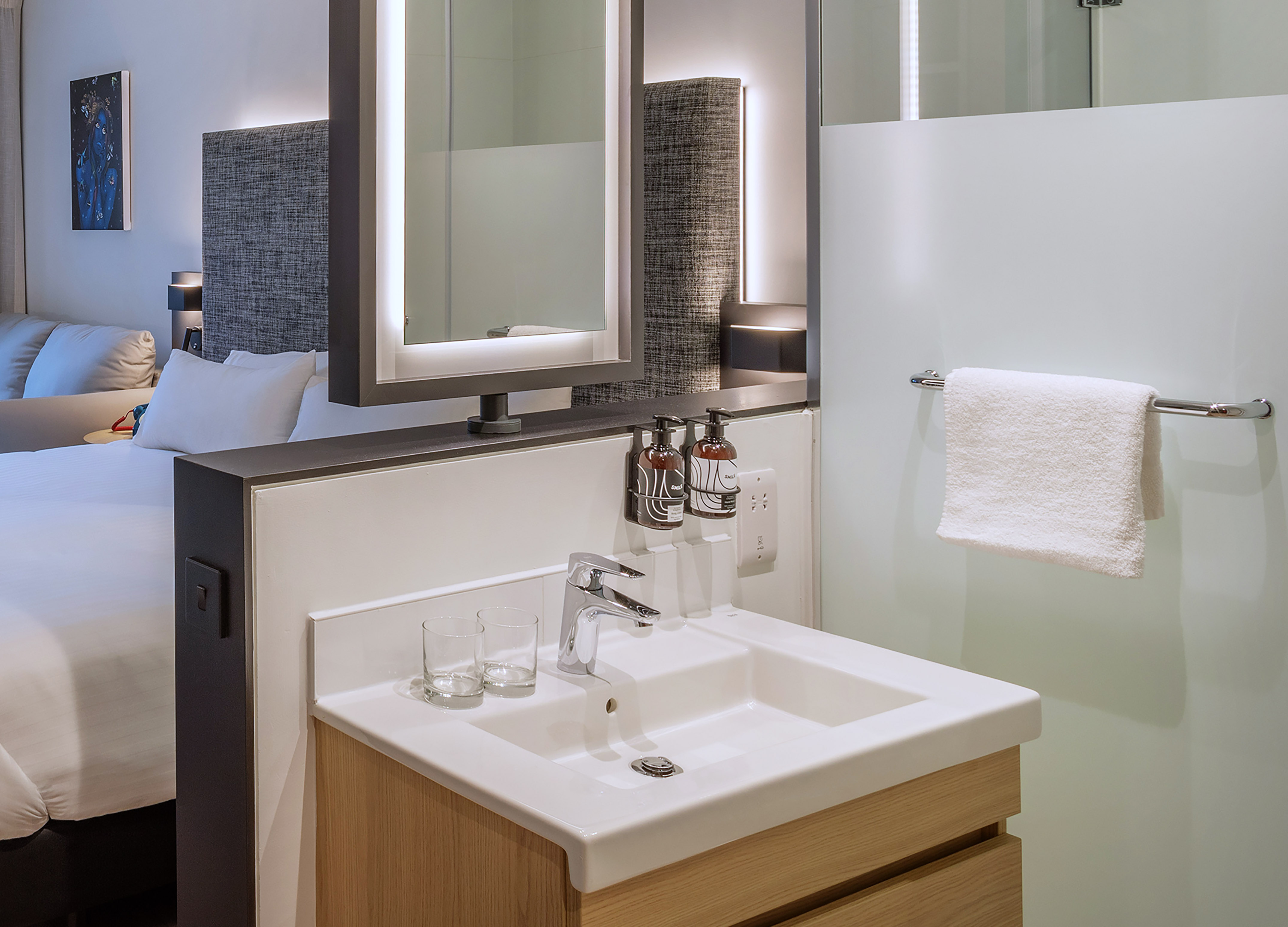 Modern hotel room: white vanity sink, backlit mirror, and hanging towel.