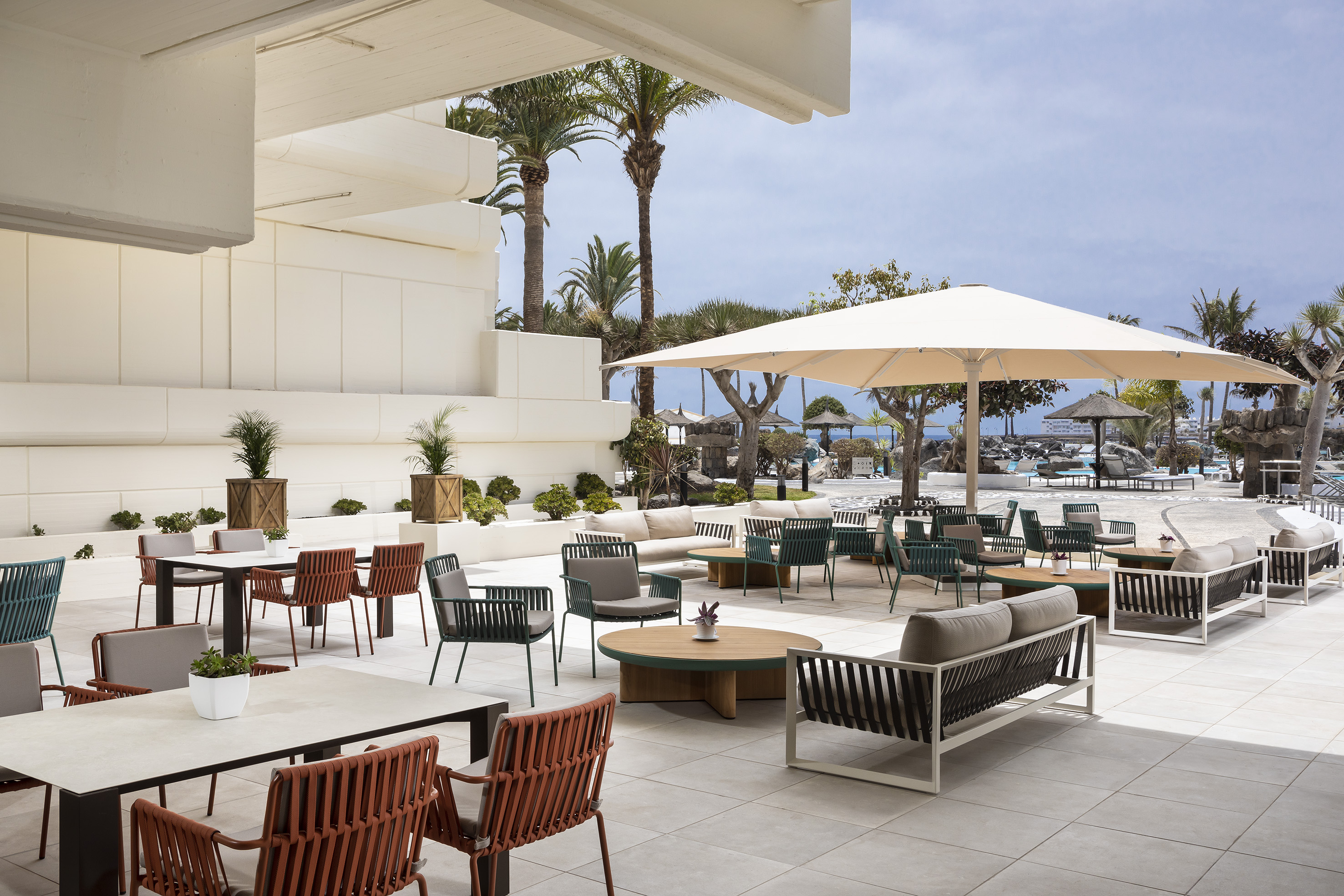 Modern resort terrace with outdoor lounge and dining furniture, palm trees.