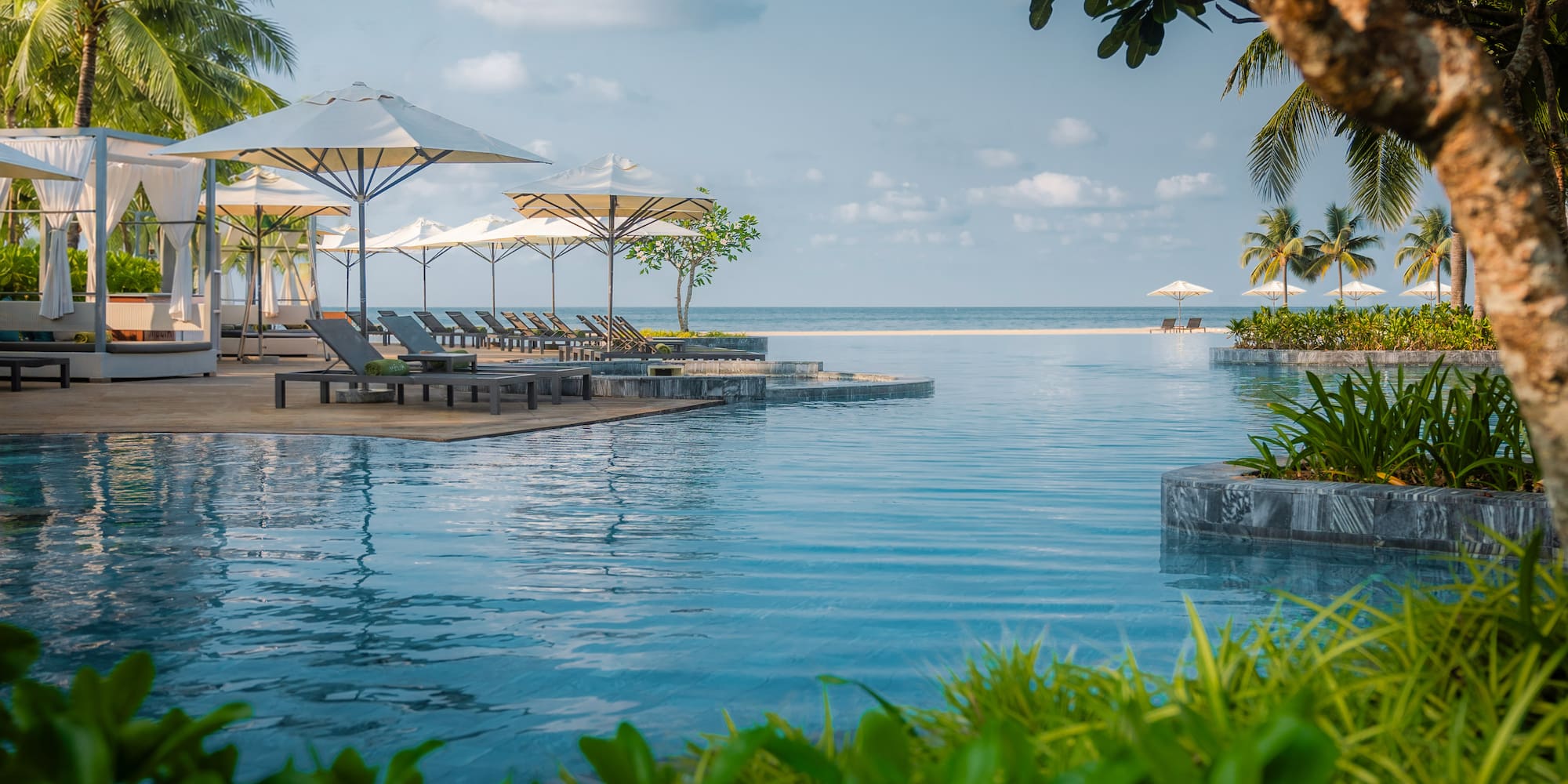 Luxury infinity pool at an oceanfront tropical resort with palm trees and lounge chairs.