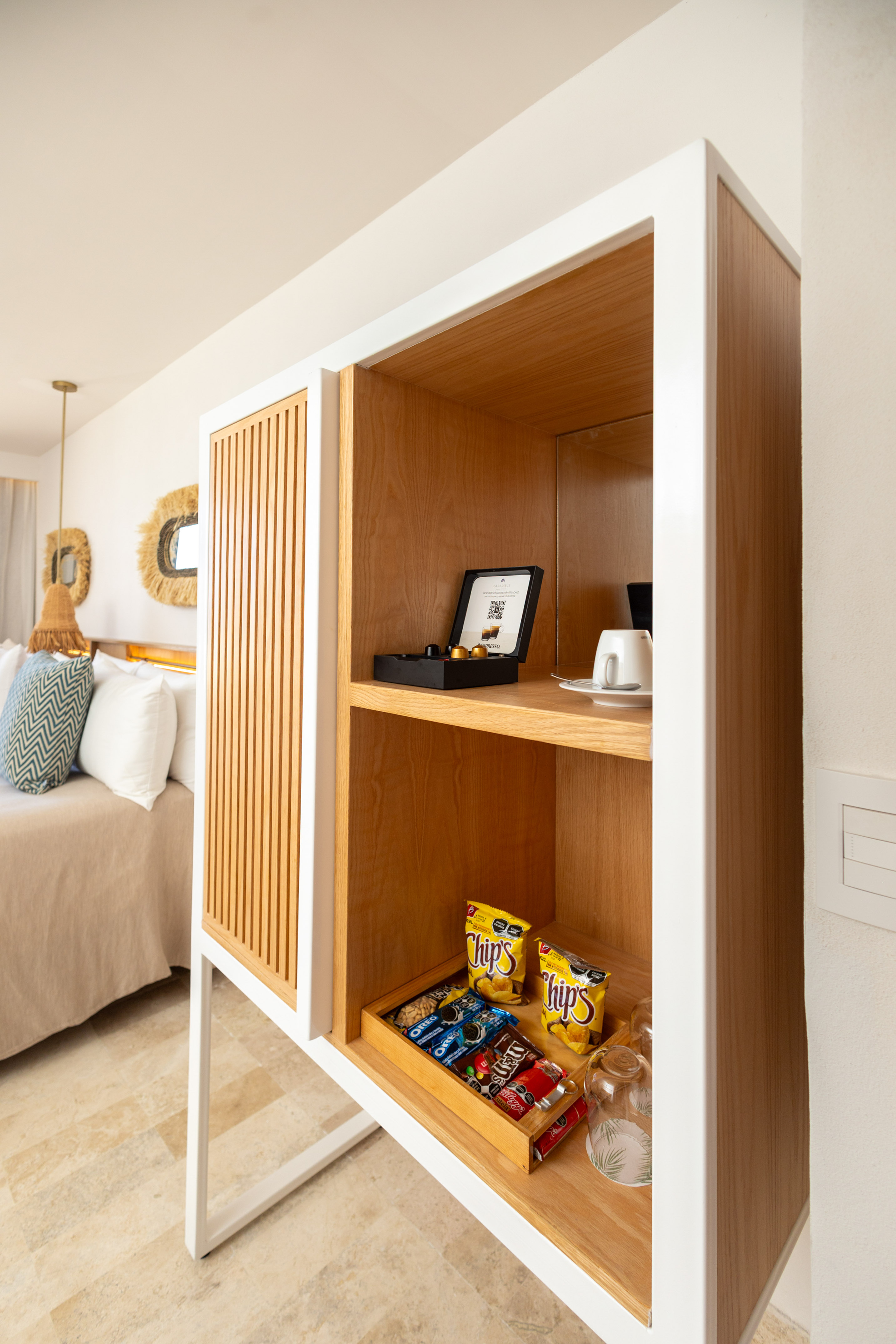 Hotel room minibar with Nespresso pods, coffee cup, and assorted snacks.