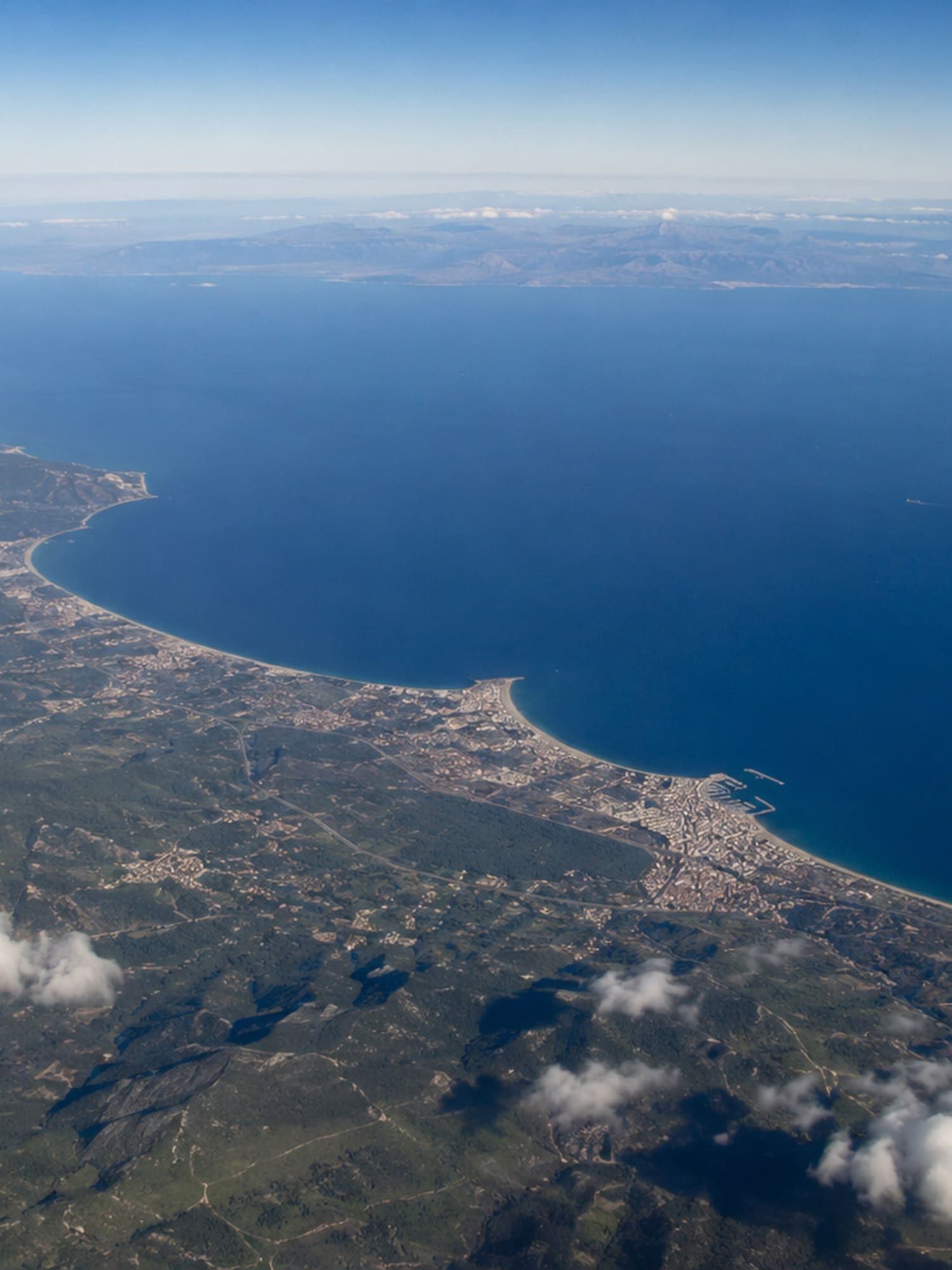 Aerial view of Mediterranean coastline, green land, coastal towns, and blue sea.