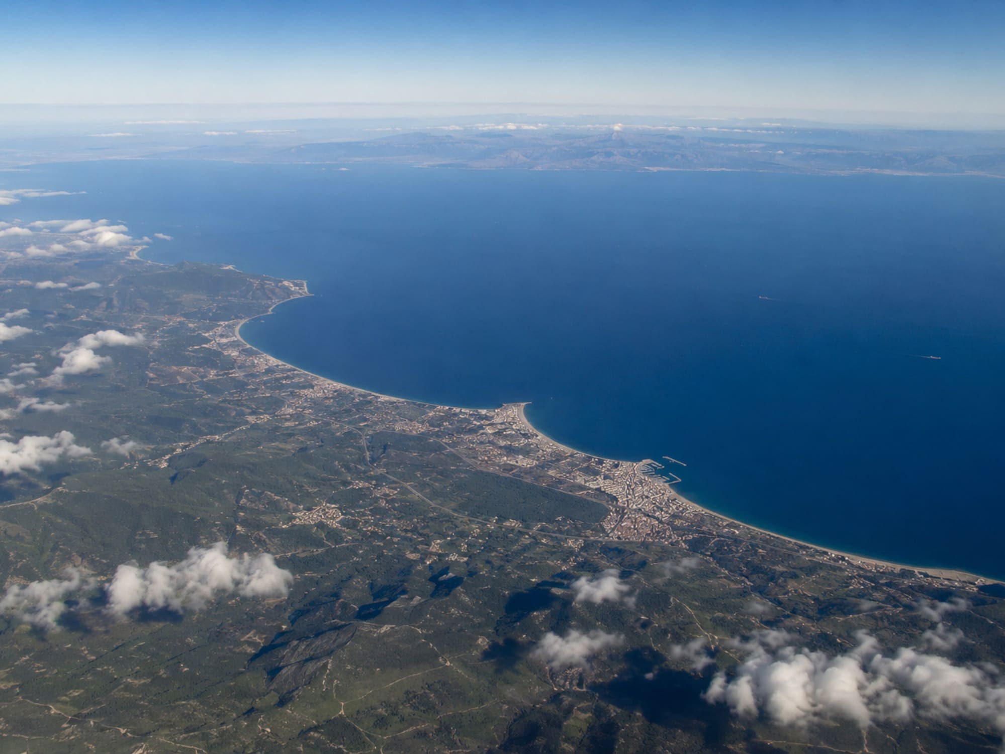 Aerial view of Mediterranean coastline, green land, coastal towns, and blue sea.