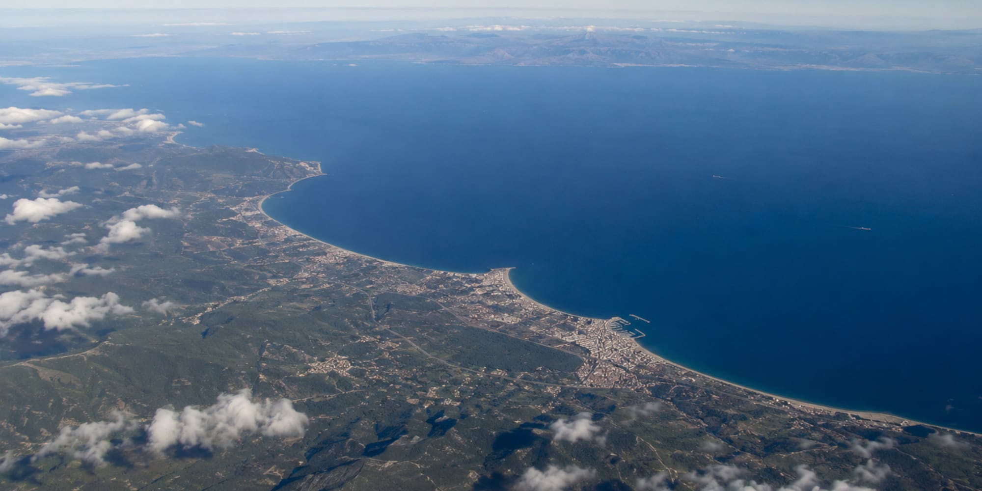 Aerial view of Mediterranean coastline, green land, coastal towns, and blue sea.
