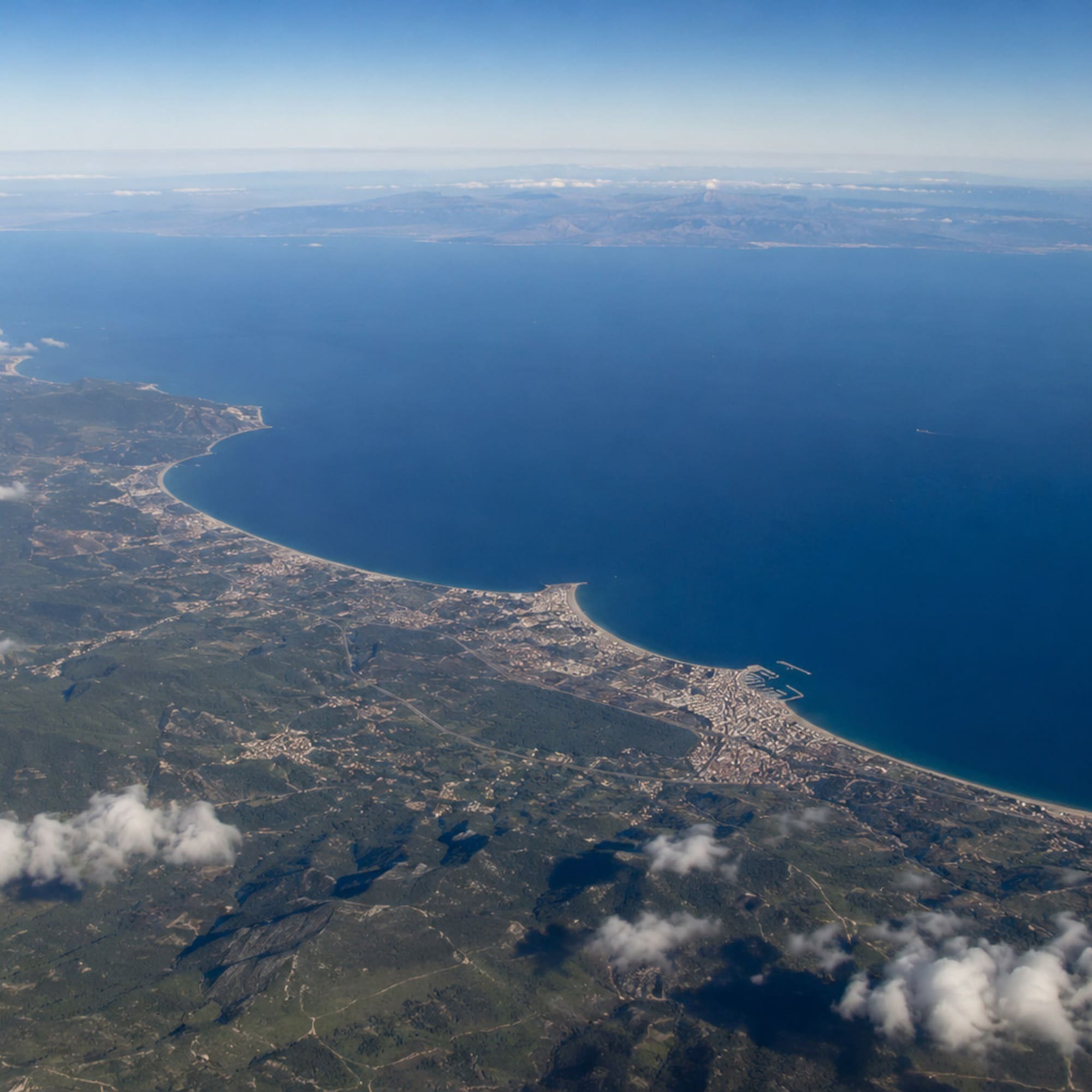 Aerial view of Mediterranean coastline, green land, coastal towns, and blue sea.