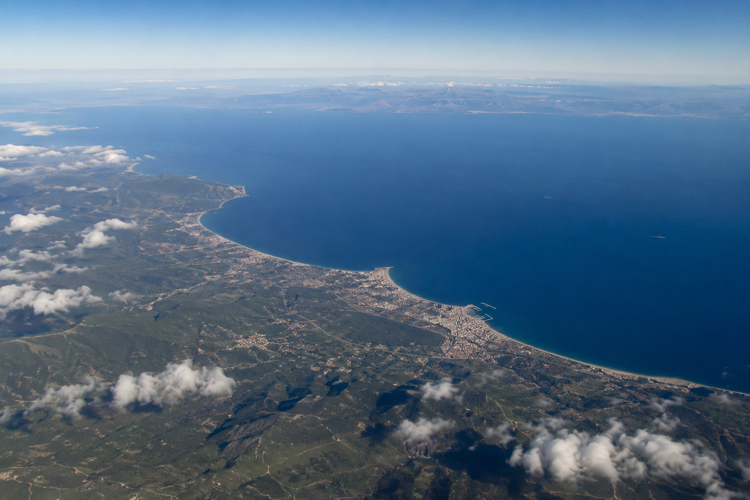 Aerial view of Mediterranean coastline, green land, coastal towns, and blue sea.