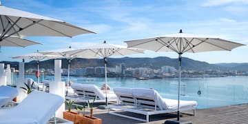 a group of white lounge chairs and umbrellas on a deck with water in the background