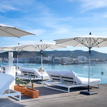 a group of white lounge chairs and umbrellas on a deck with water in the background