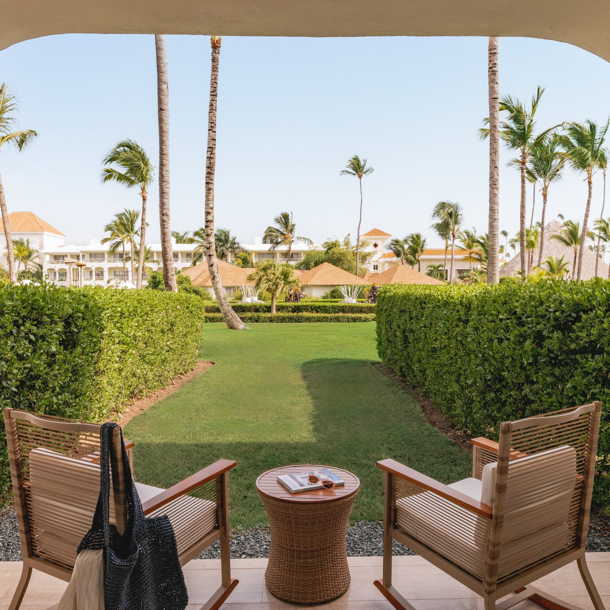 Tropical resort patio overlooking garden with chairs and palm trees.