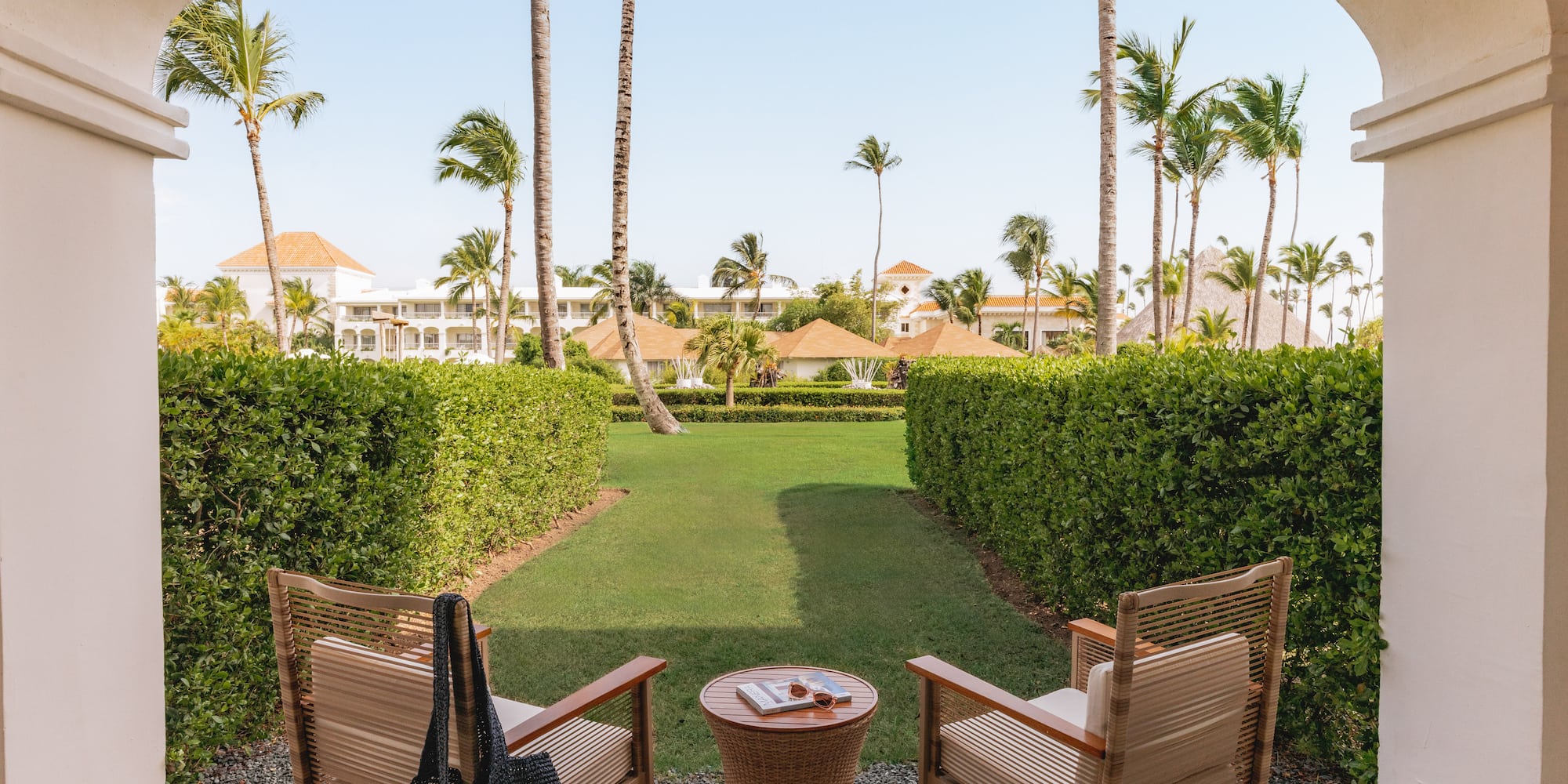 Tropical resort patio overlooking garden with chairs and palm trees.