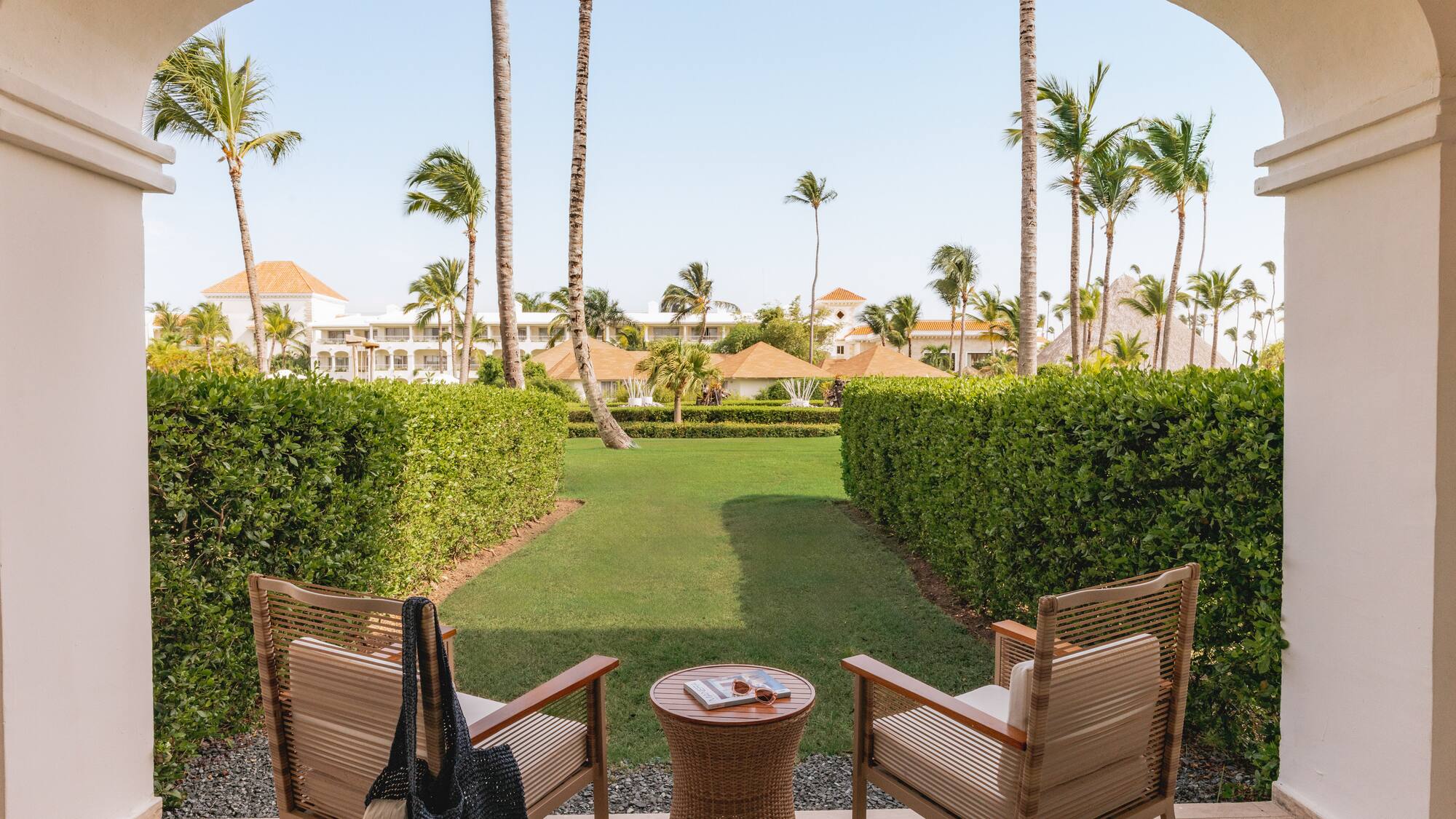 Tropical resort patio overlooking garden with chairs and palm trees.