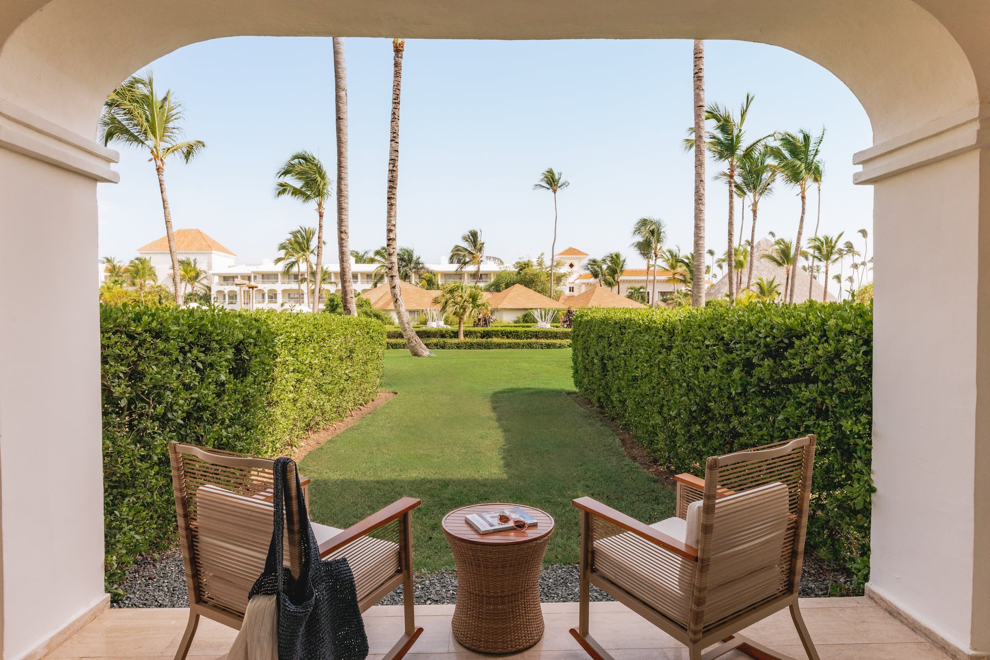 Tropical resort patio overlooking garden with chairs and palm trees.
