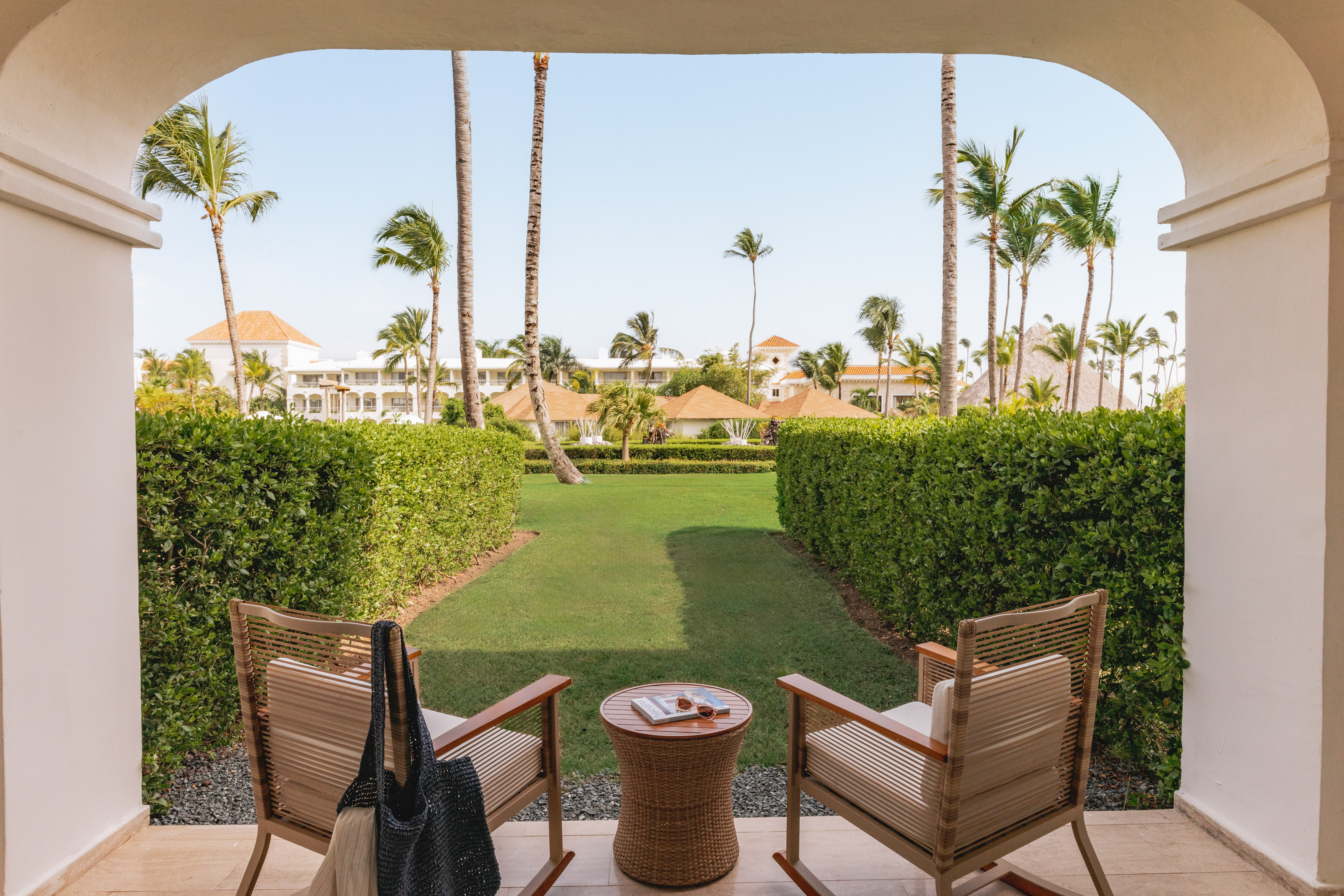 Tropical resort patio overlooking garden with chairs and palm trees.