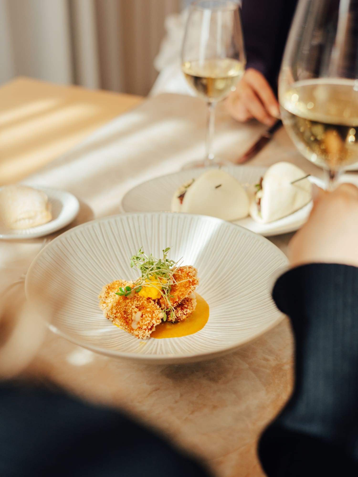 Crispy fried appetizer with microgreens, white wine, and bao buns at a restaurant.