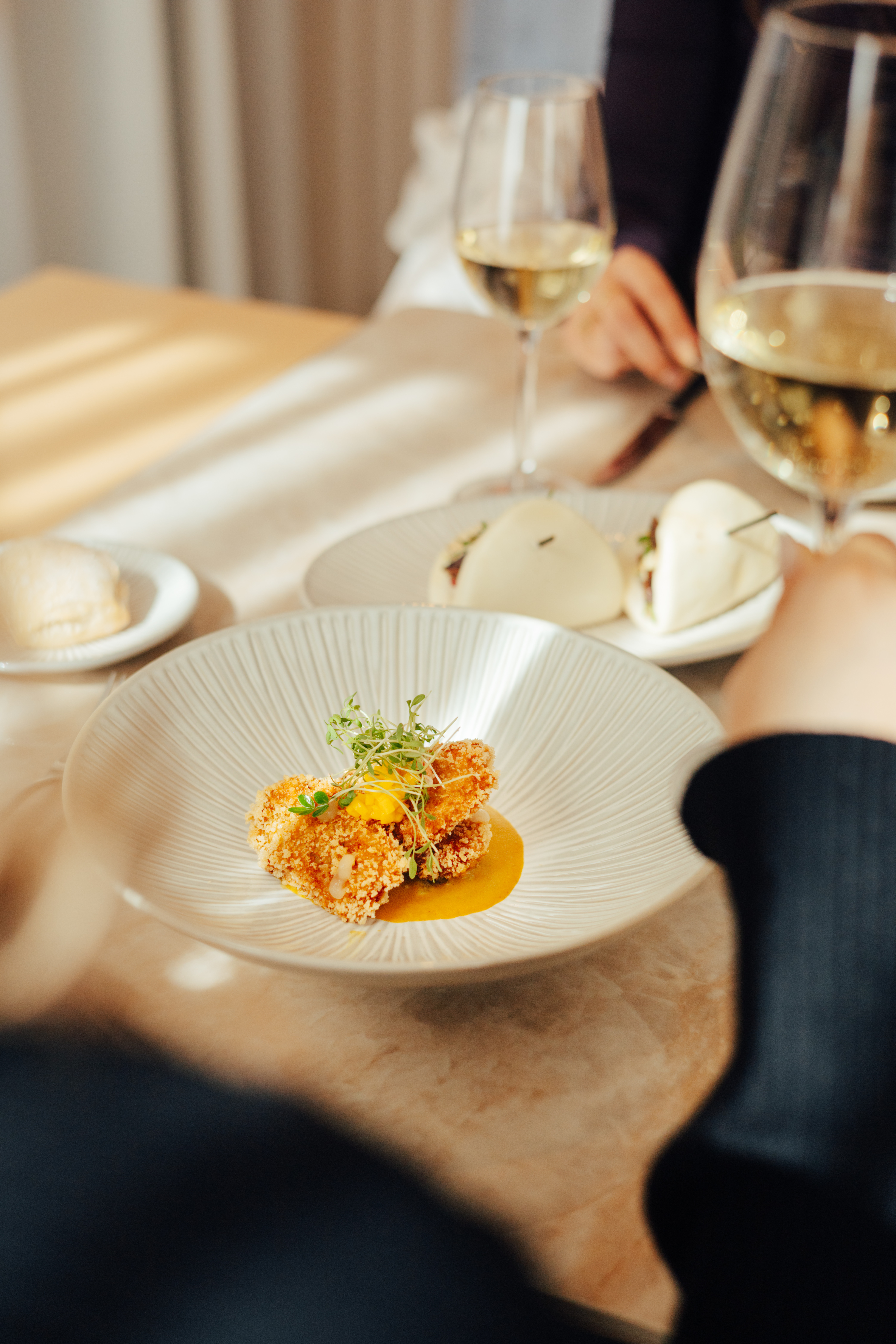 Crispy fried appetizer with microgreens, white wine, and bao buns at a restaurant.