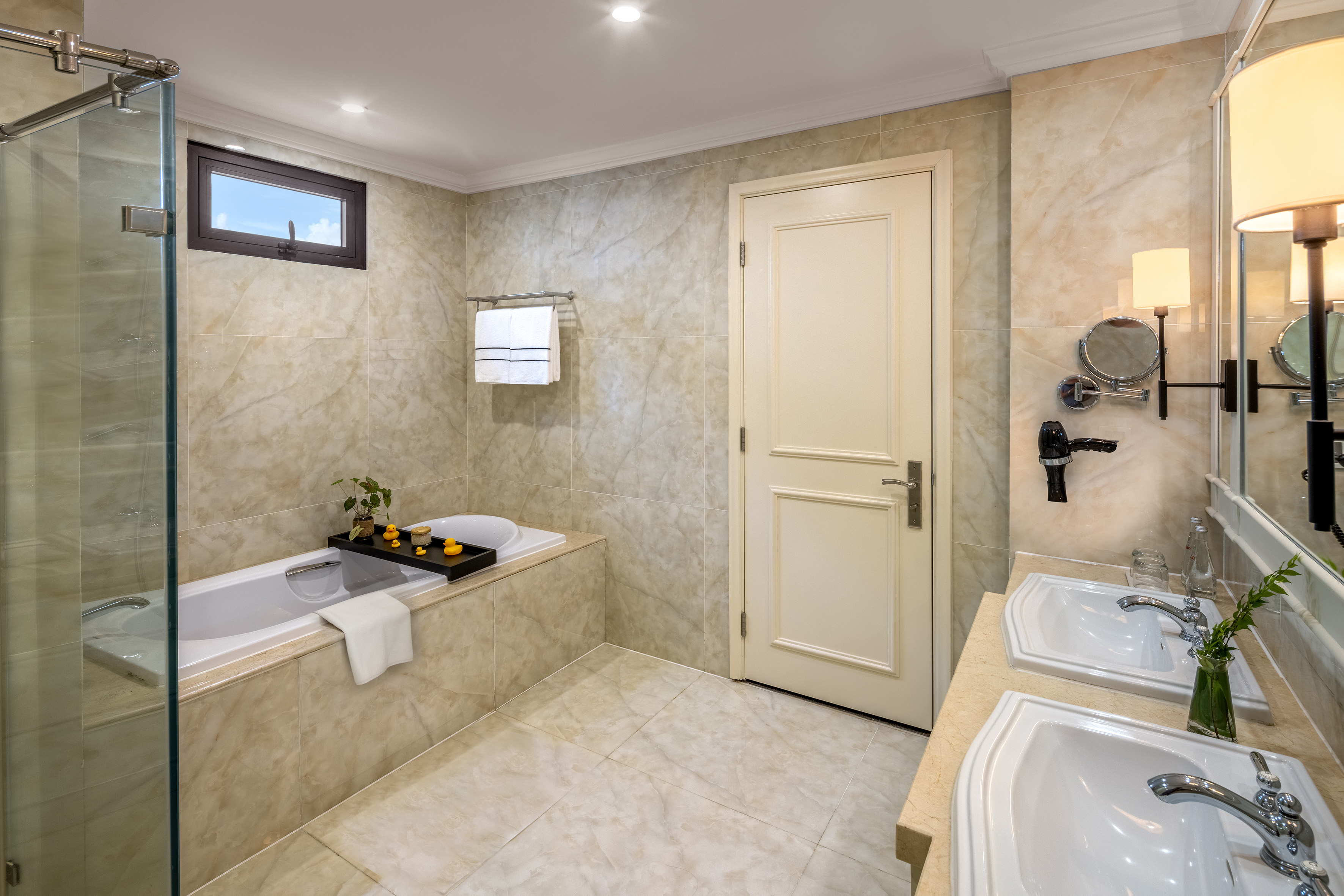 Tiled bathroom with bathtub, glass shower, and double vanity.